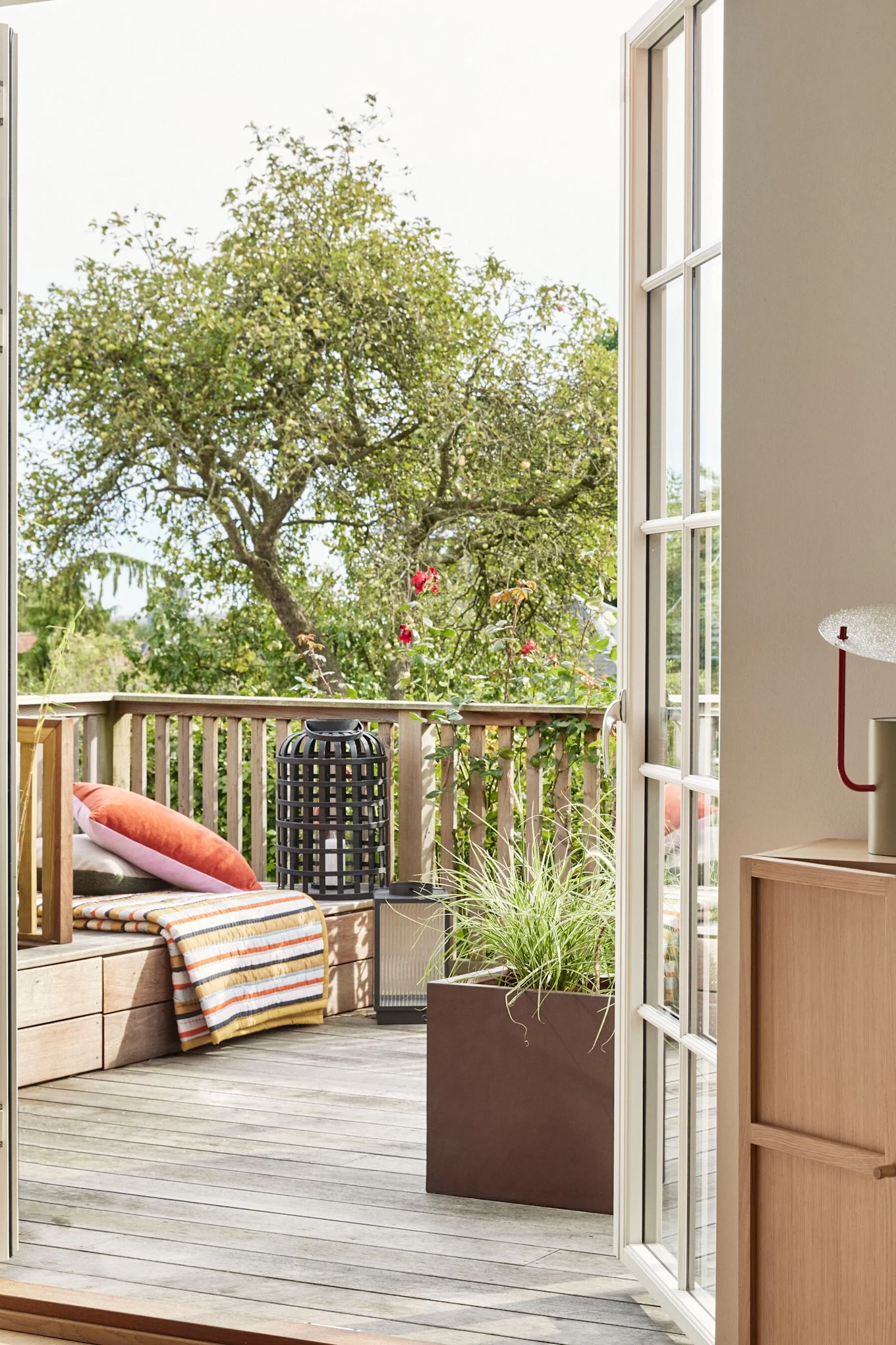 Decoración boho para balcones: la manta a rayas de Hübsch Interior sobre un balcón de madera.