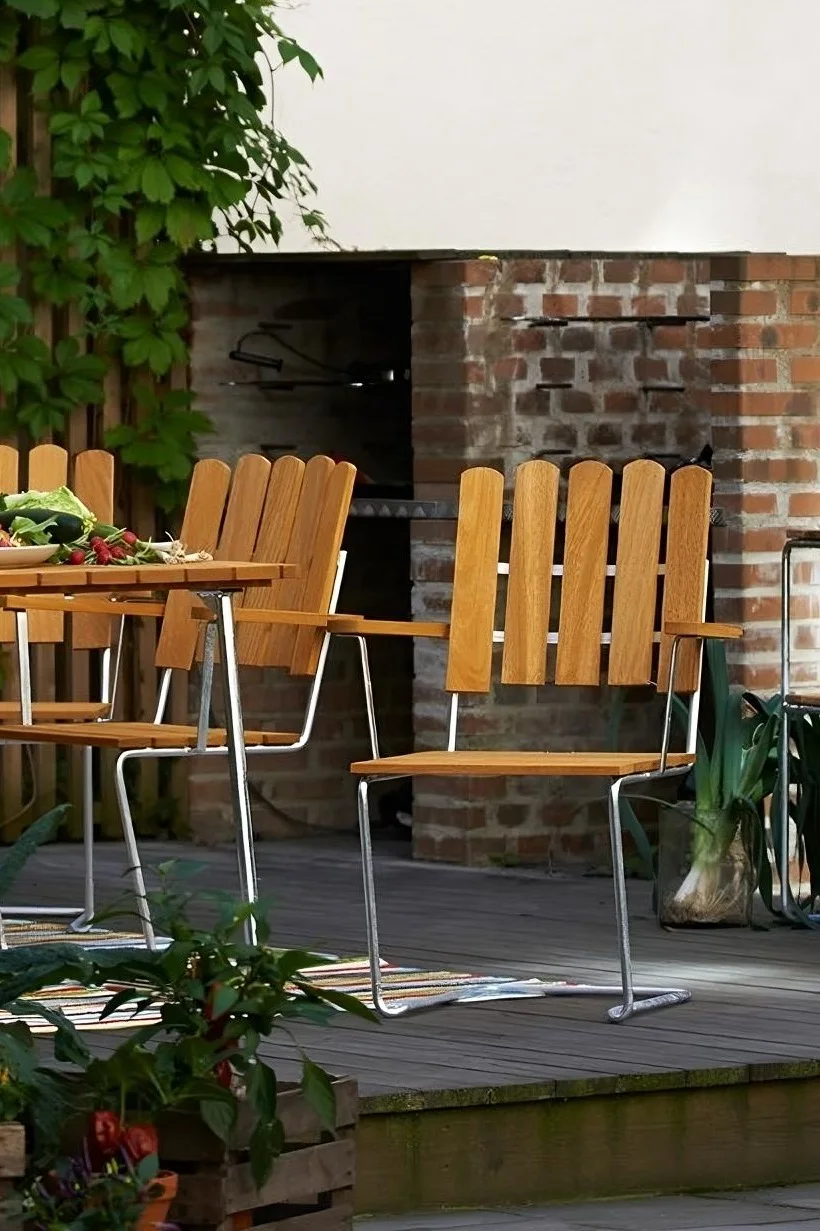 La silla A2 de Grythyttan está fabricada de teca y acero, vista aquí en una terraza, por lo que encaja perfectamente en las tendencias de mobiliario de jardín de 2025.