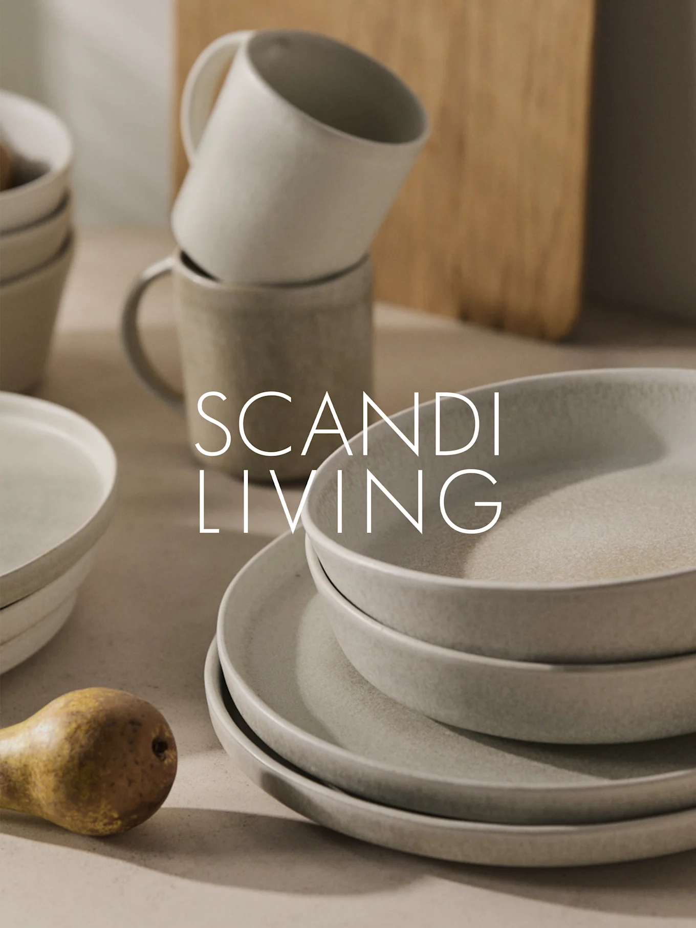 Vajilla de cerámica beige apilada, tazas y una pera con superposición de "SCANDI LIVING".