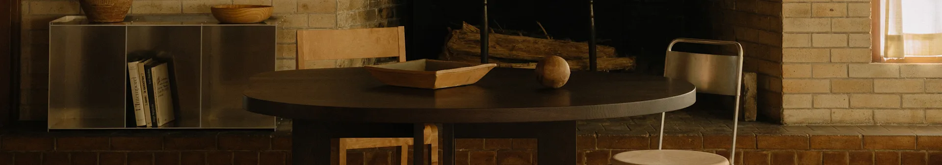 Un acogedor comedor con una mesa redonda de madera oscura, un cuenco de madera, un objeto ovalado, sillas y una chimenea.