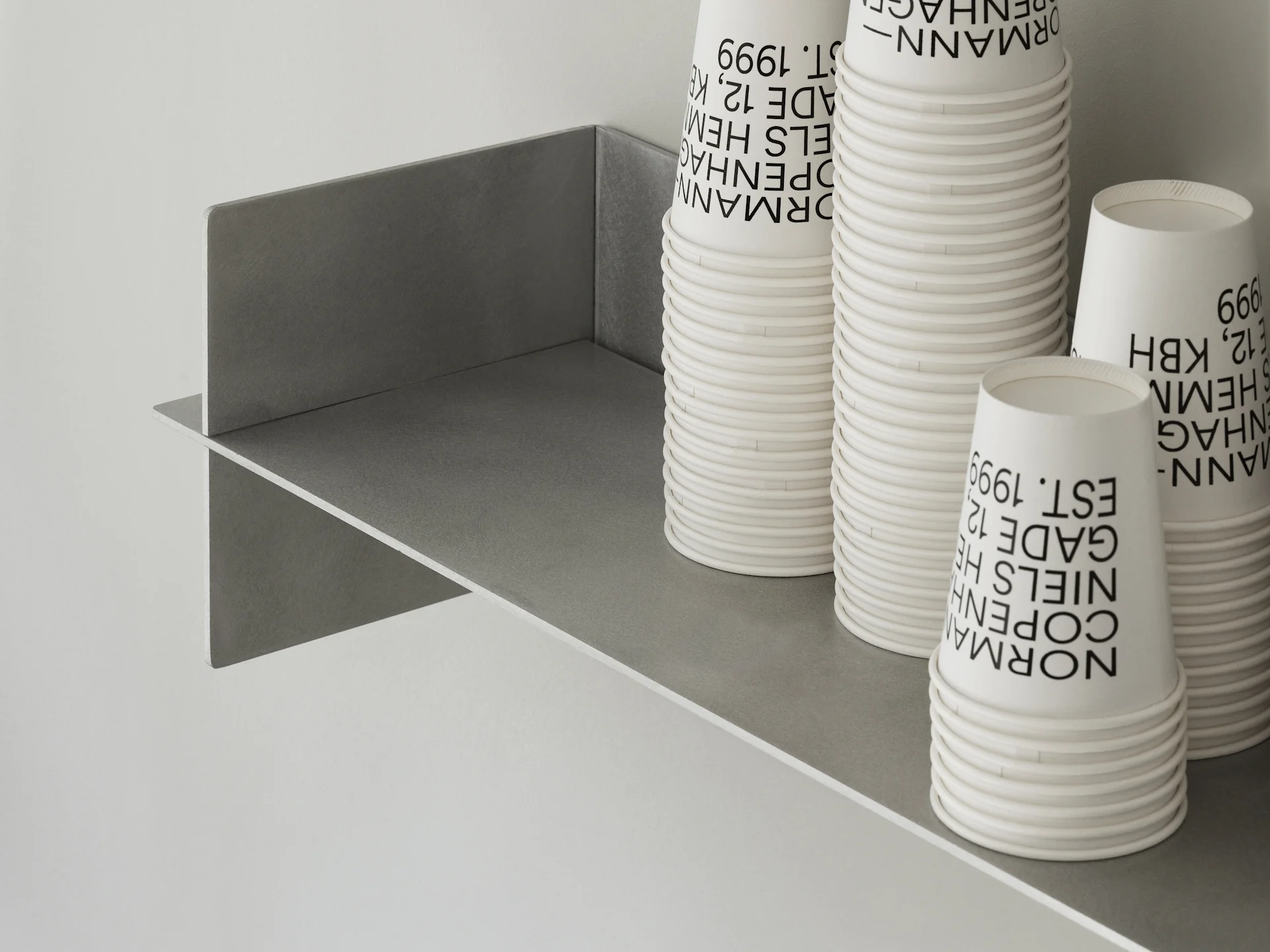 Vasos de papel blancos apilados con texto negro en un estante gris.