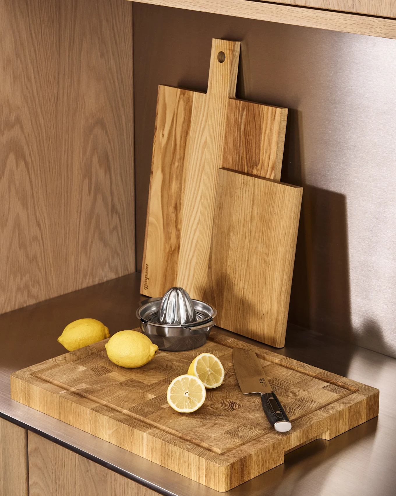 Encimera de cocina con tres tablas de cortar de madera, un exprimidor de limones metálico, limones enteros y partidos, y un cuchillo.