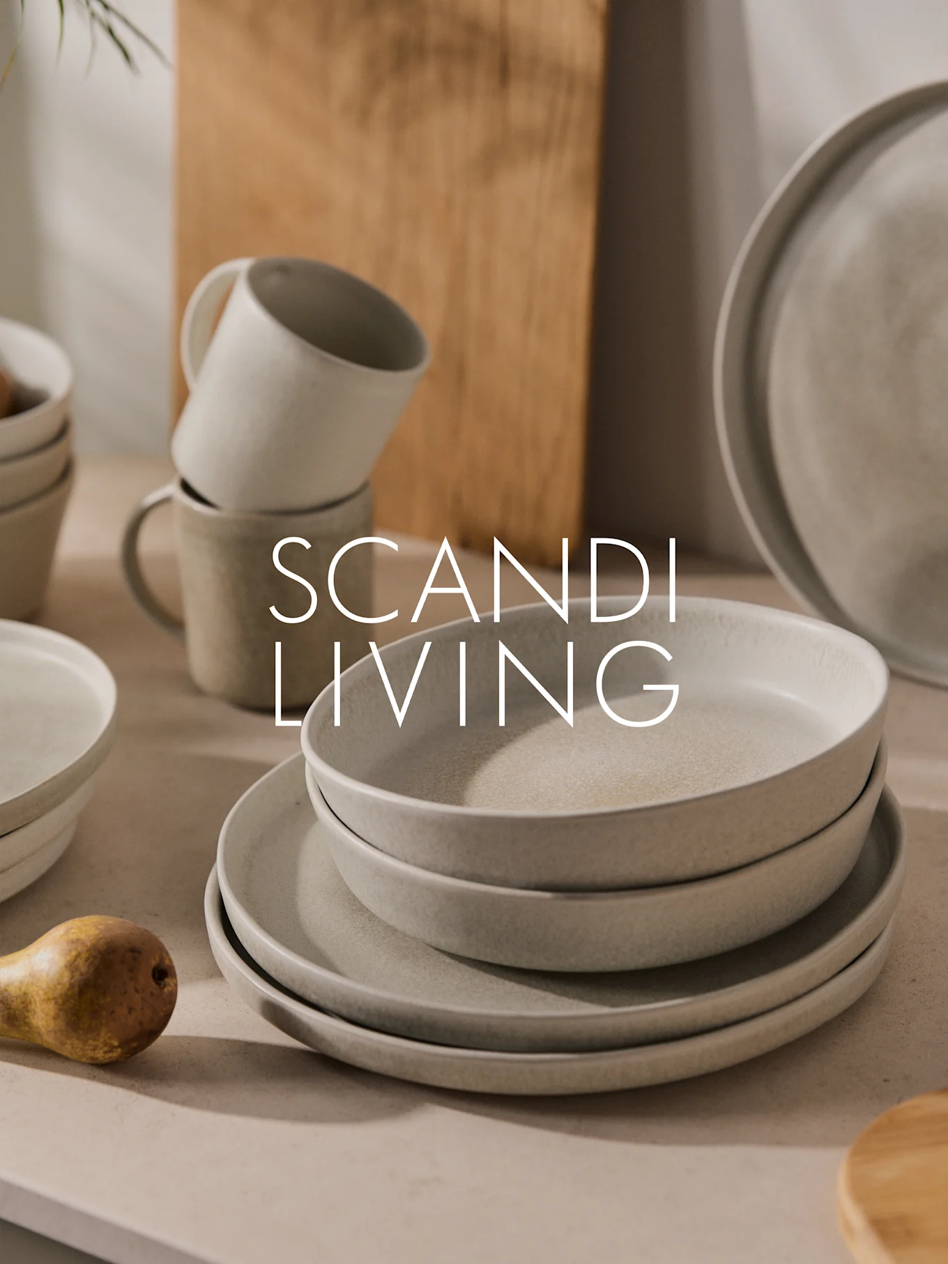Pila de platos, cuencos y tazas de cerámica clara moteada con una pera. Texto: SCANDI LIVING.