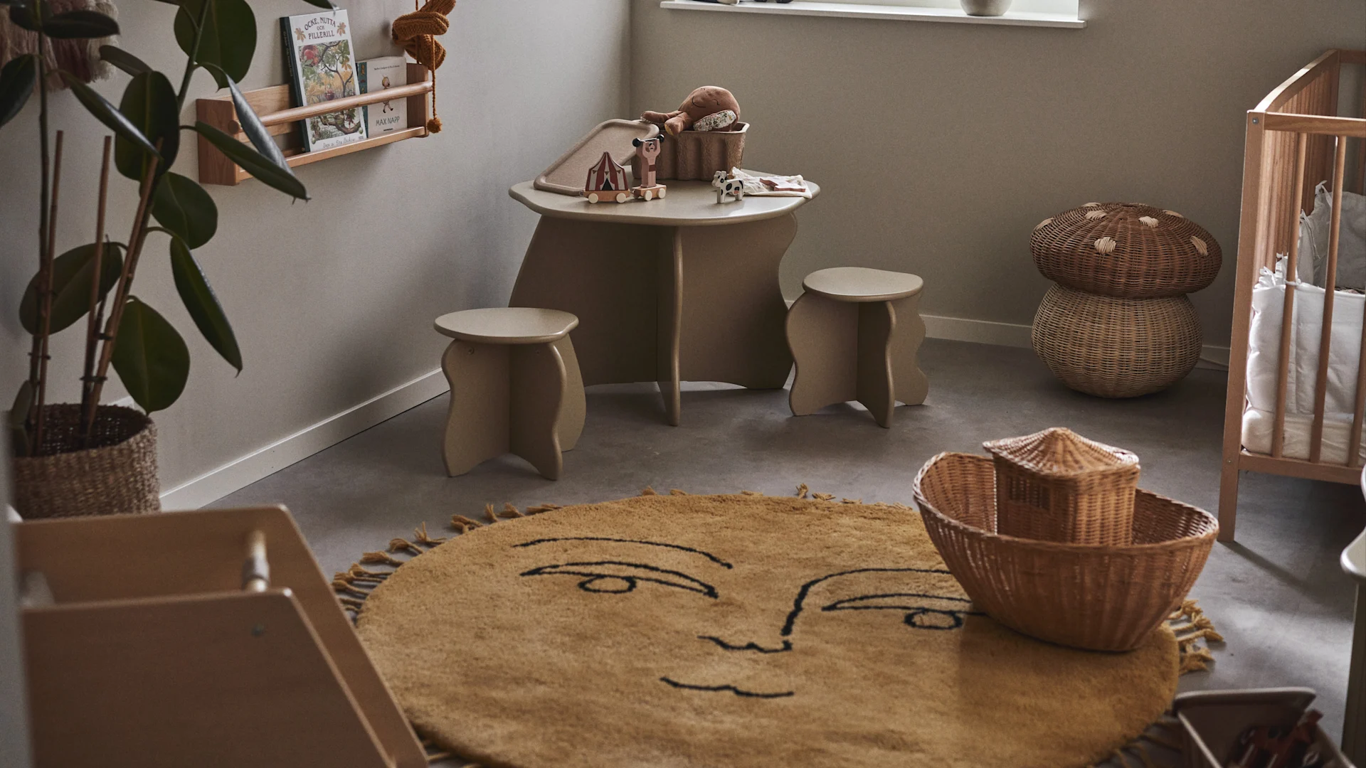 Colocar una alfombra grande y suave en el centro de la habitación crea una zona de juego acogedora y amplia a la hora de decorar la habitación infantil. Aquí la alfombra con forma de sol Sun de Ferm Living en una habitación infantil con mesa, taburetes y cuna.