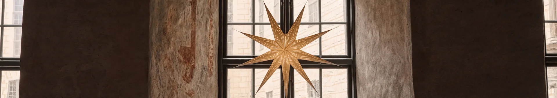Una linterna con forma de estrella cuelga en una ventana arqueada, con patrones ornamentados en las paredes de piedra y el arco.