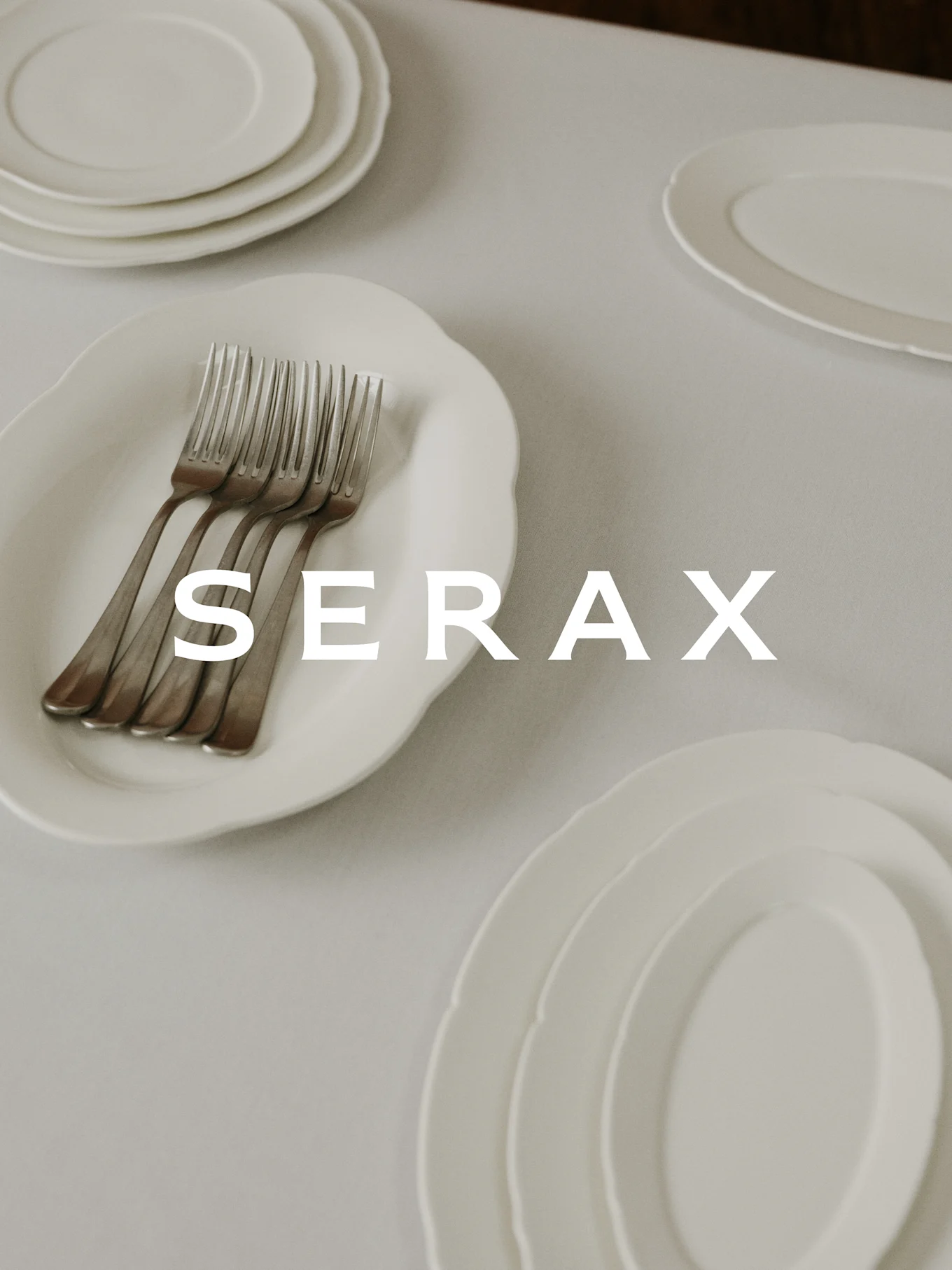 Mesa puesta con platos blancos y tenedores, con el texto 'SERAX' superpuesto.