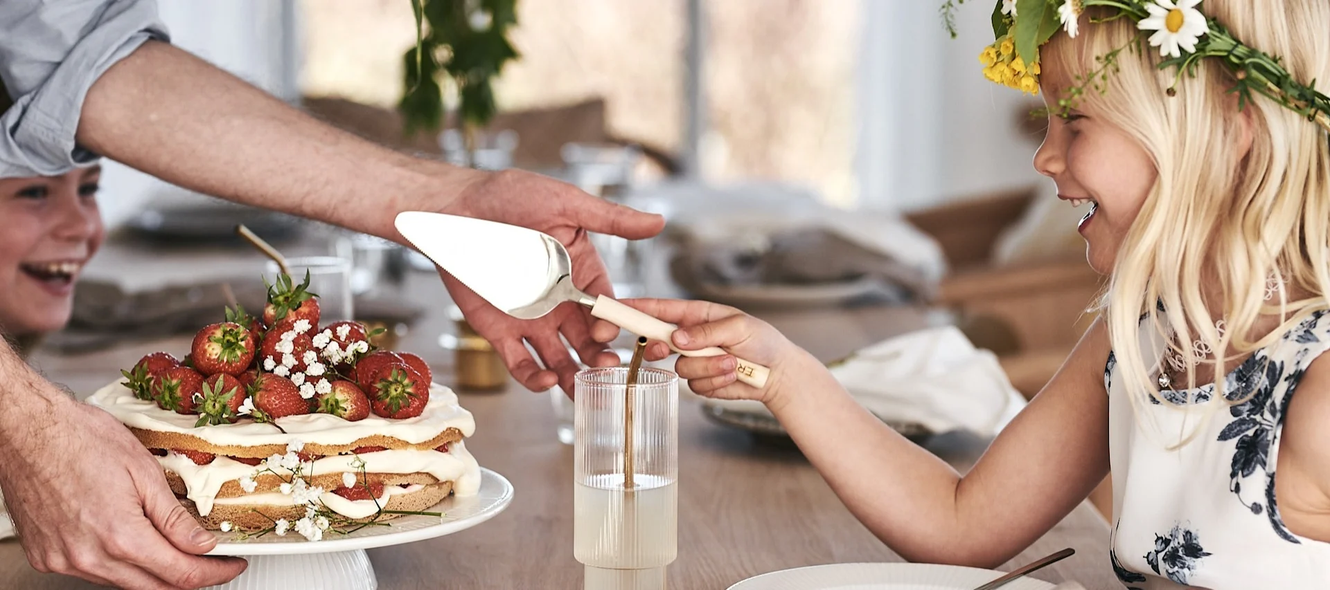 Descubre ideas suecas para fiestas de verano. Una persona corta una tarta tradicional de fresas mientras lleva una corona de flores de Midsummer.