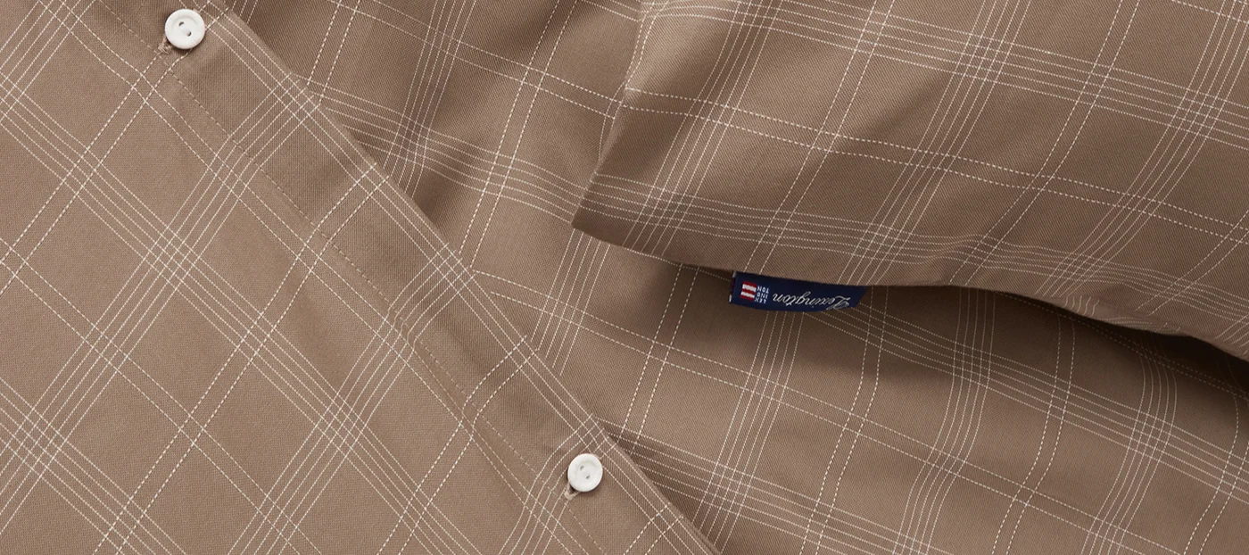 Primer plano de tela marrón con patrón de cuadros blancos, con dos botones blancos y una etiqueta azul de Lexington.
