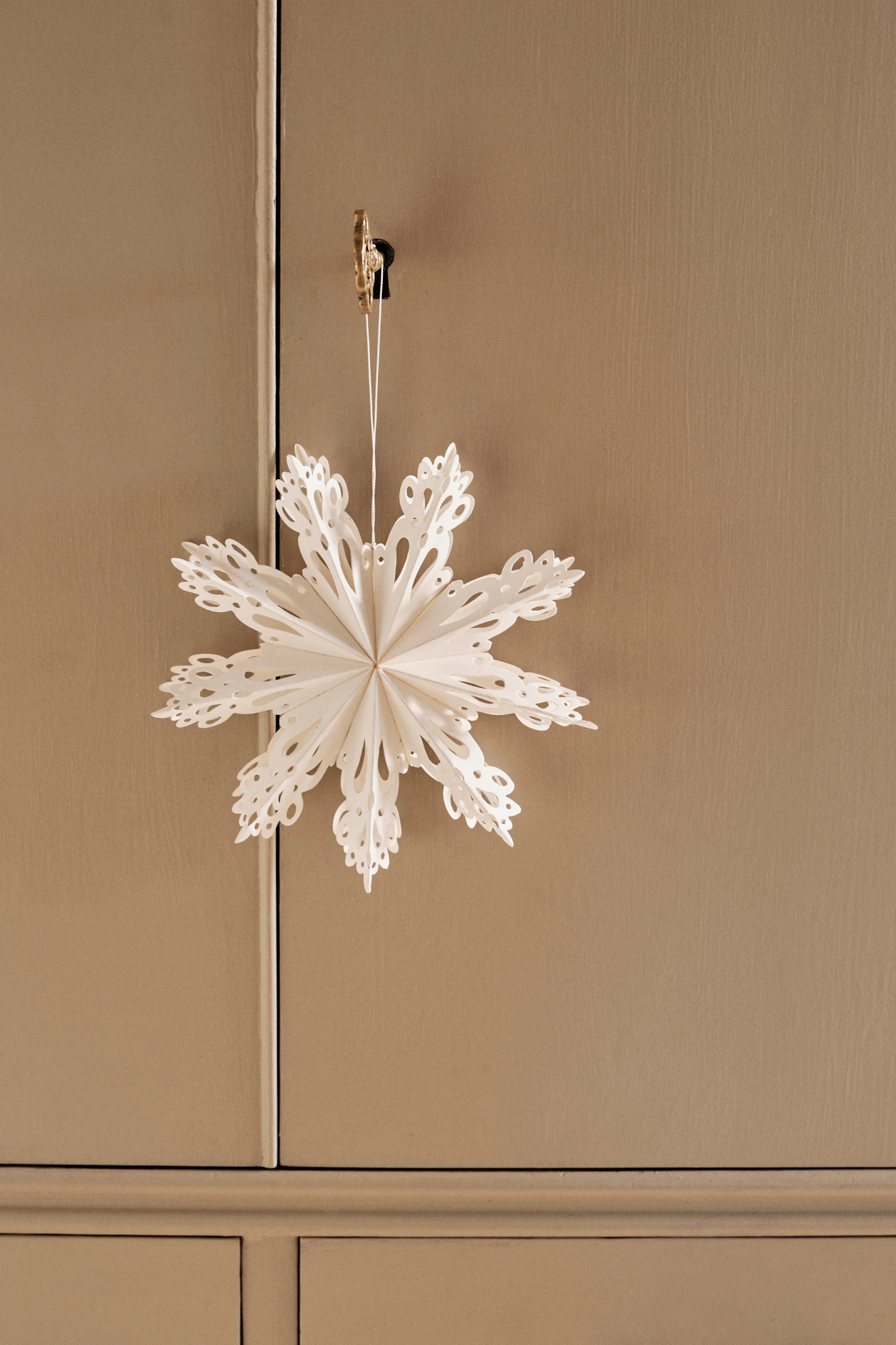 Un copo de nieve de papel blanco, recortado con gran detalle, cuelga de una pequeña llave dorada en la cerradura de un armario de madera de color marrón claro.
