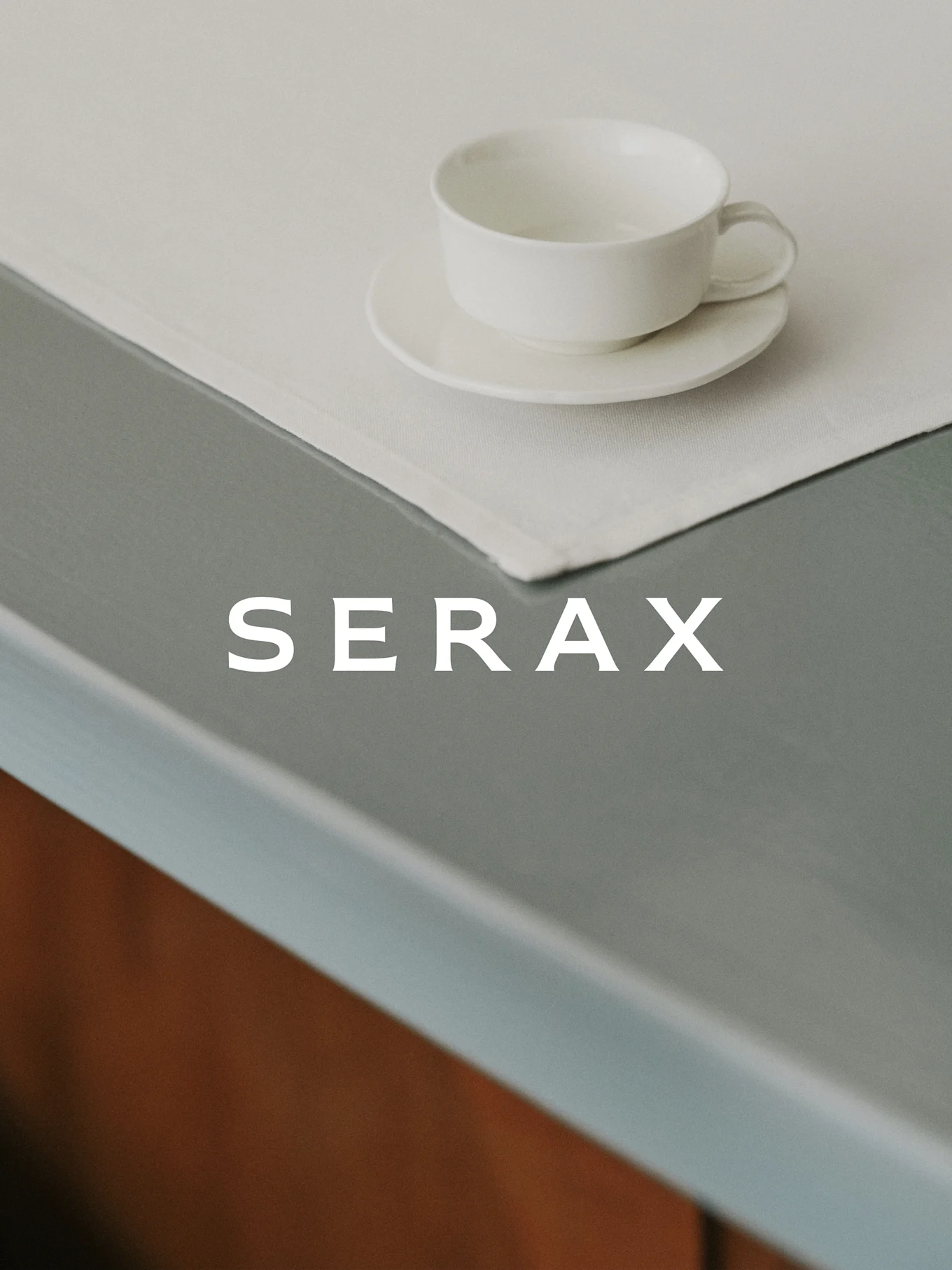 Una taza de té blanca y su platillo sobre un mantel individual de lino claro en una mesa gris con la palabra SERAX.