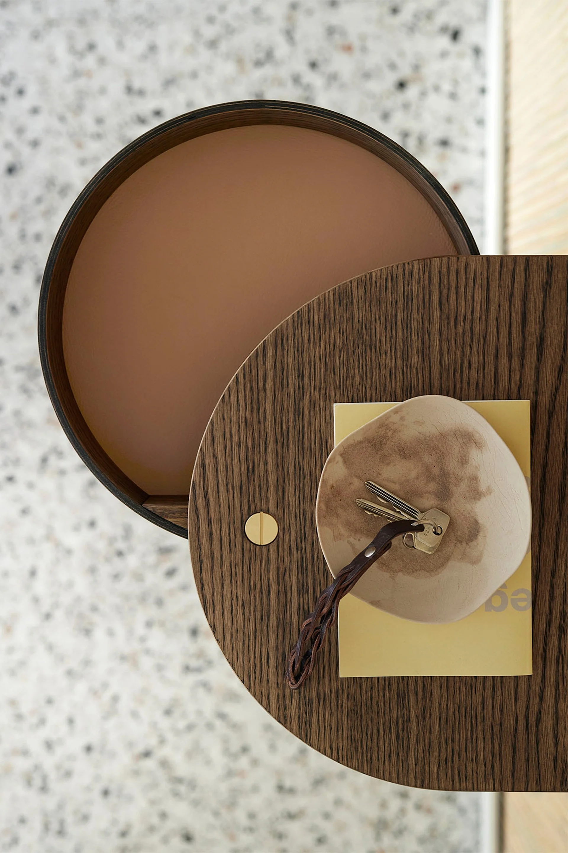 Vista aérea de una mesa de madera circular con llaves en un plato y un libro amarillo.