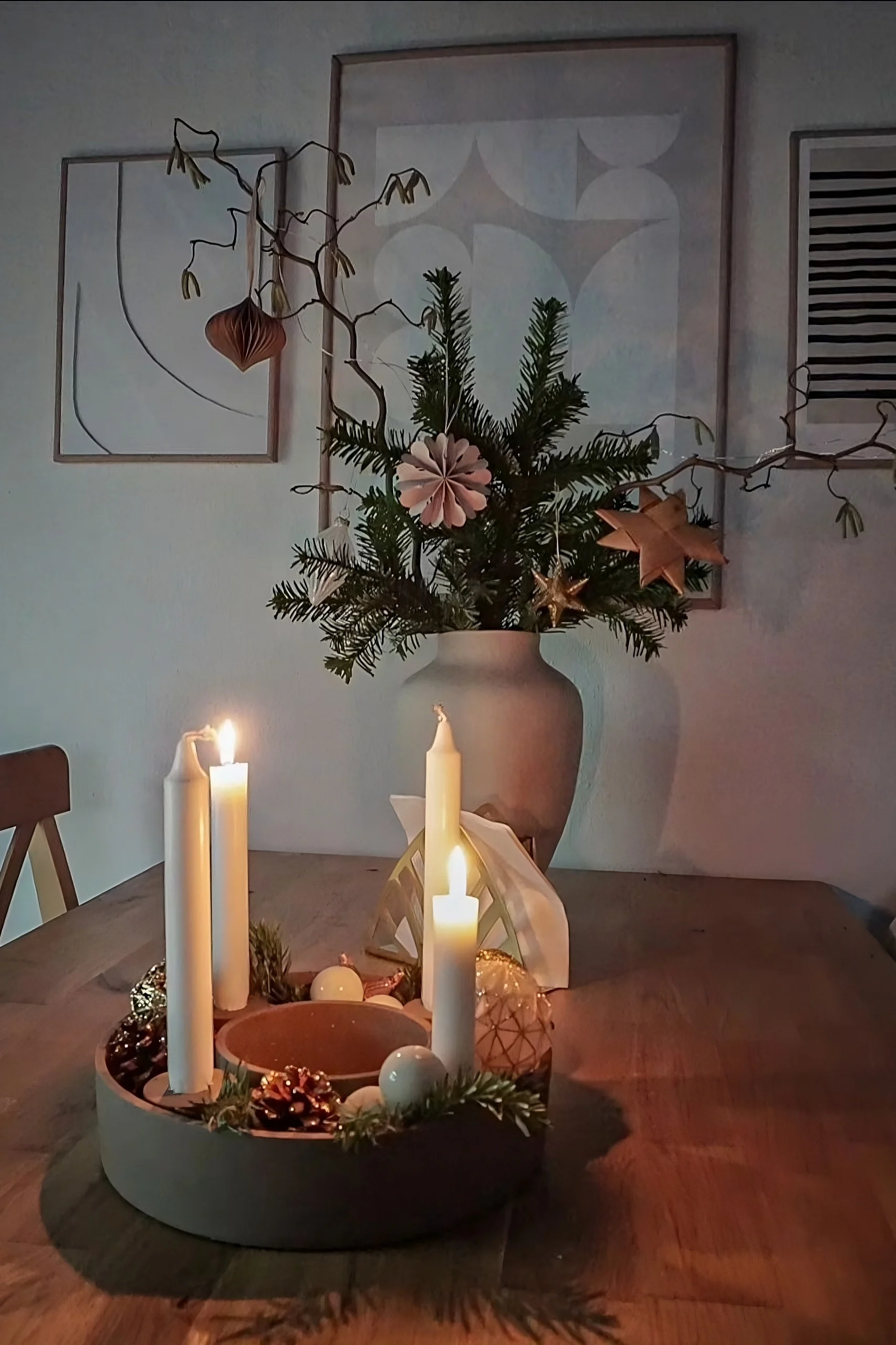 Sobre una mesa de madera se encuentra el portavelas The Ring de House Doctor, decorado con piñas y ramas de abeto.