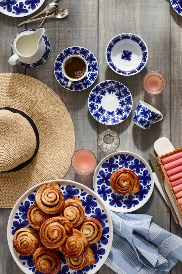 Los rollos de canela suecos son los pasteles para fika más famosos, incluso más allá de las fronteras de Suecia. Aquí los puedes ver en la vajilla Mon Ami de Rörstrand, servidos en una mesa al aire libre con un sombrero de verano.