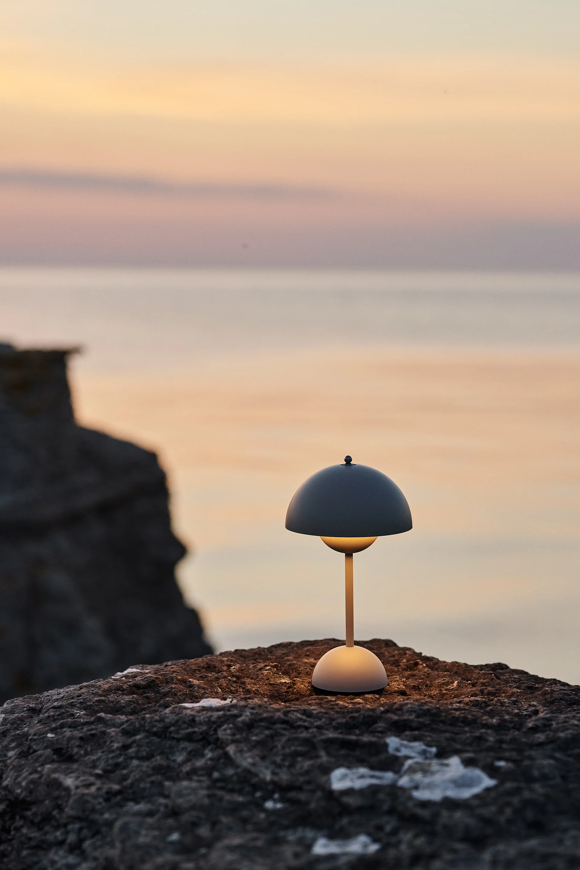 La lámpara inalámbrica Flowerpot de &Tradition, colocada sobre las rocas de la playa, es un imprescindible del verano que no te puedes perder. 