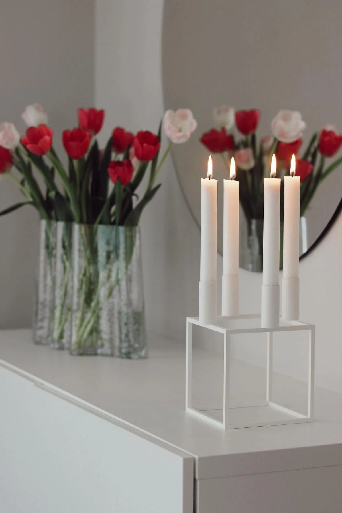 Aquí, el portavelas blanco Kubus con cuatro velas de Audo Copenhagen sobre una cómoda, detrás el jarrón Gry de Cooee Design con tulipanes en casa de @susannfrustol.