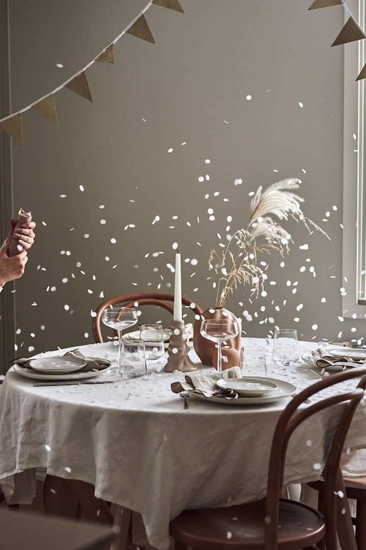Cómo organizar una fiesta con el ambiente perfecto. Aquí ves una mesa decorada con un petardo de fiesta recién explotado y el confeti cayendo sobre la mesa.