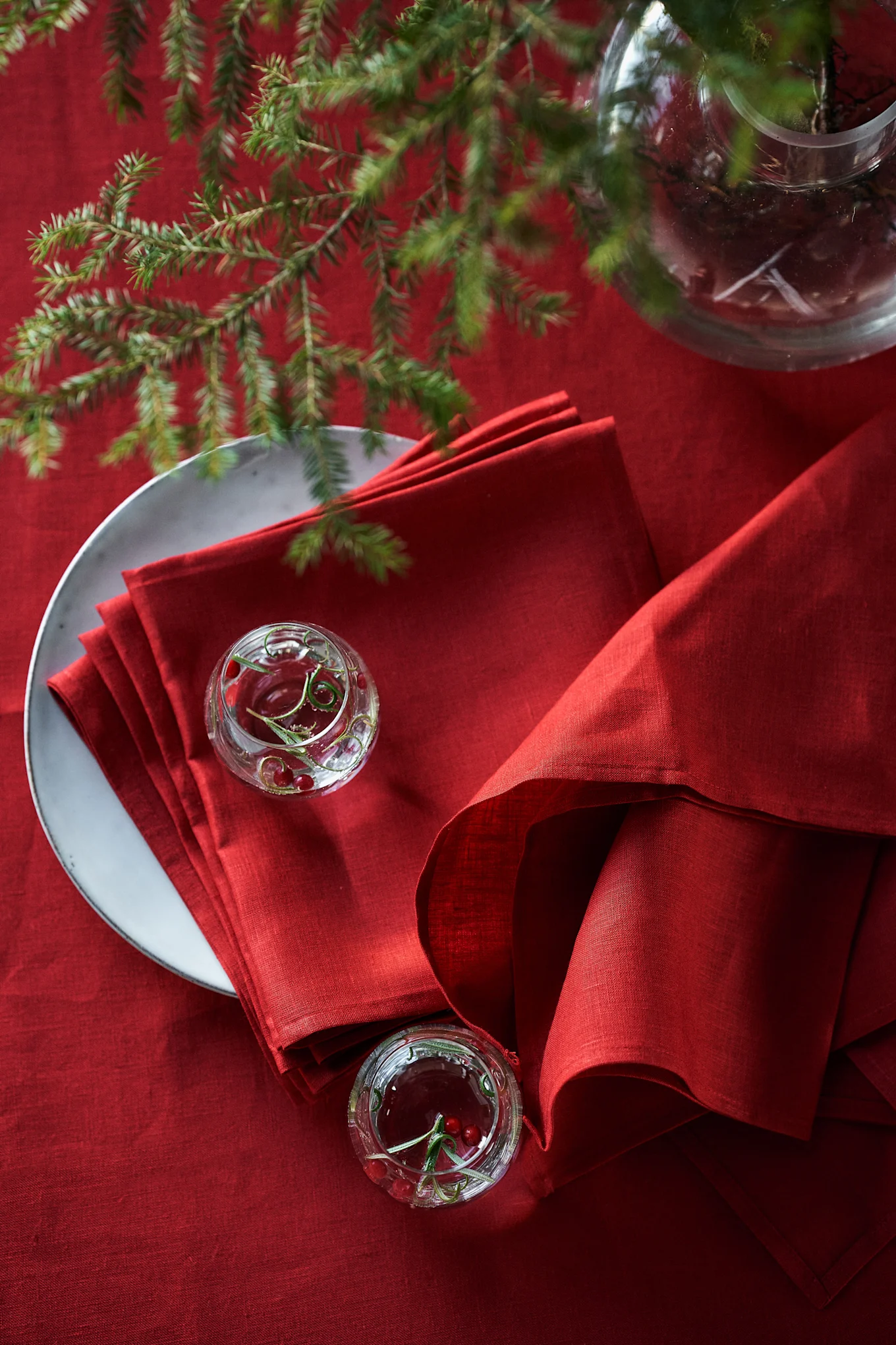 Mesa festiva roja con servilletas de lino rojas apiladas en un plato, pequeños cuencos de cristal con arándanos rojos y ramas de pino.