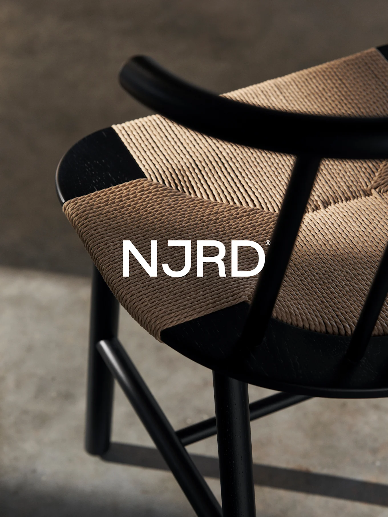 Primer plano de una silla negra con un asiento tejido de color marrón claro, con el logotipo blanco 'NJRD'.