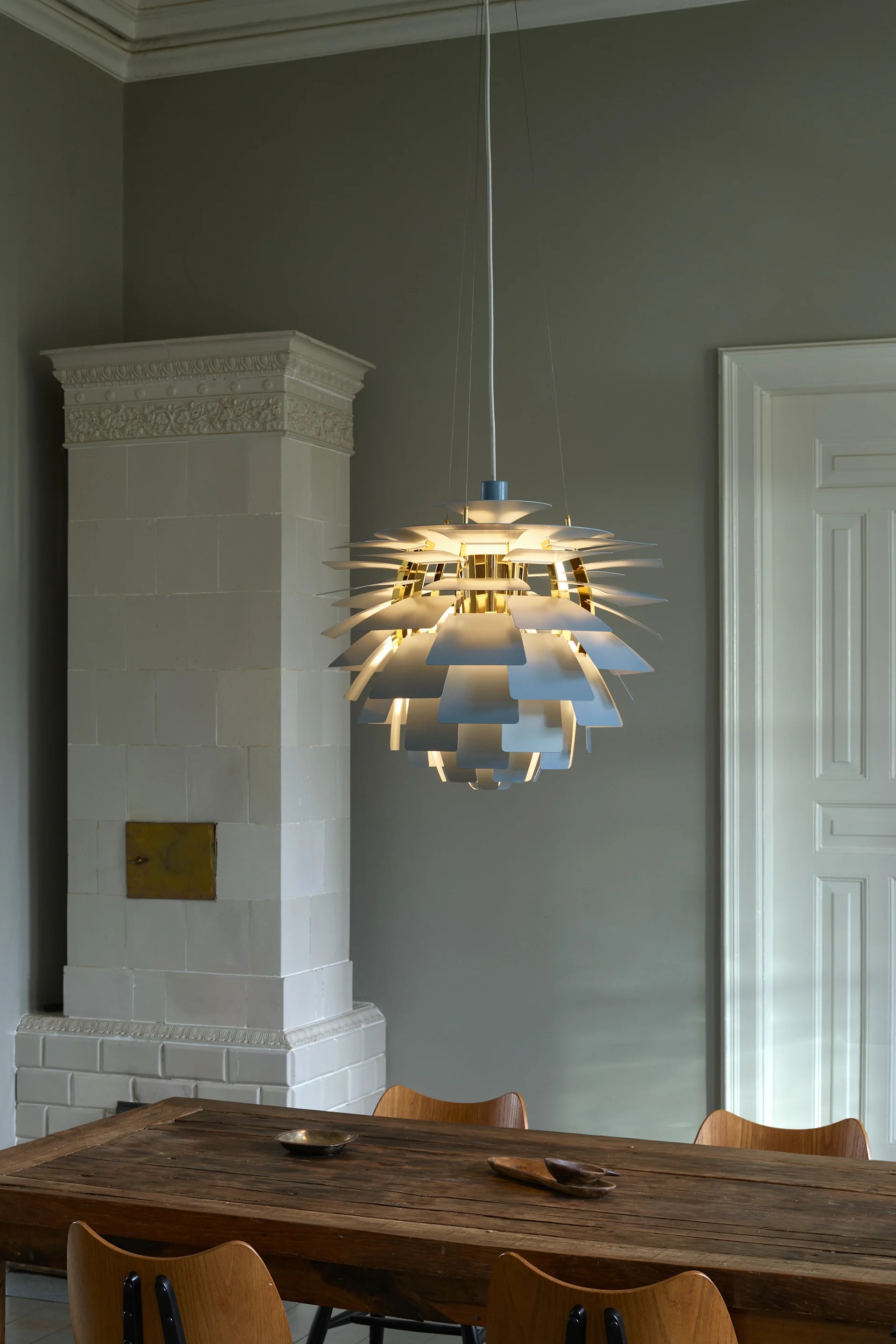 Una lámpara de techo ilumiando de múltiples capas con detalles blancos y dorados, sobre una mesa de comedor de madera rústica.