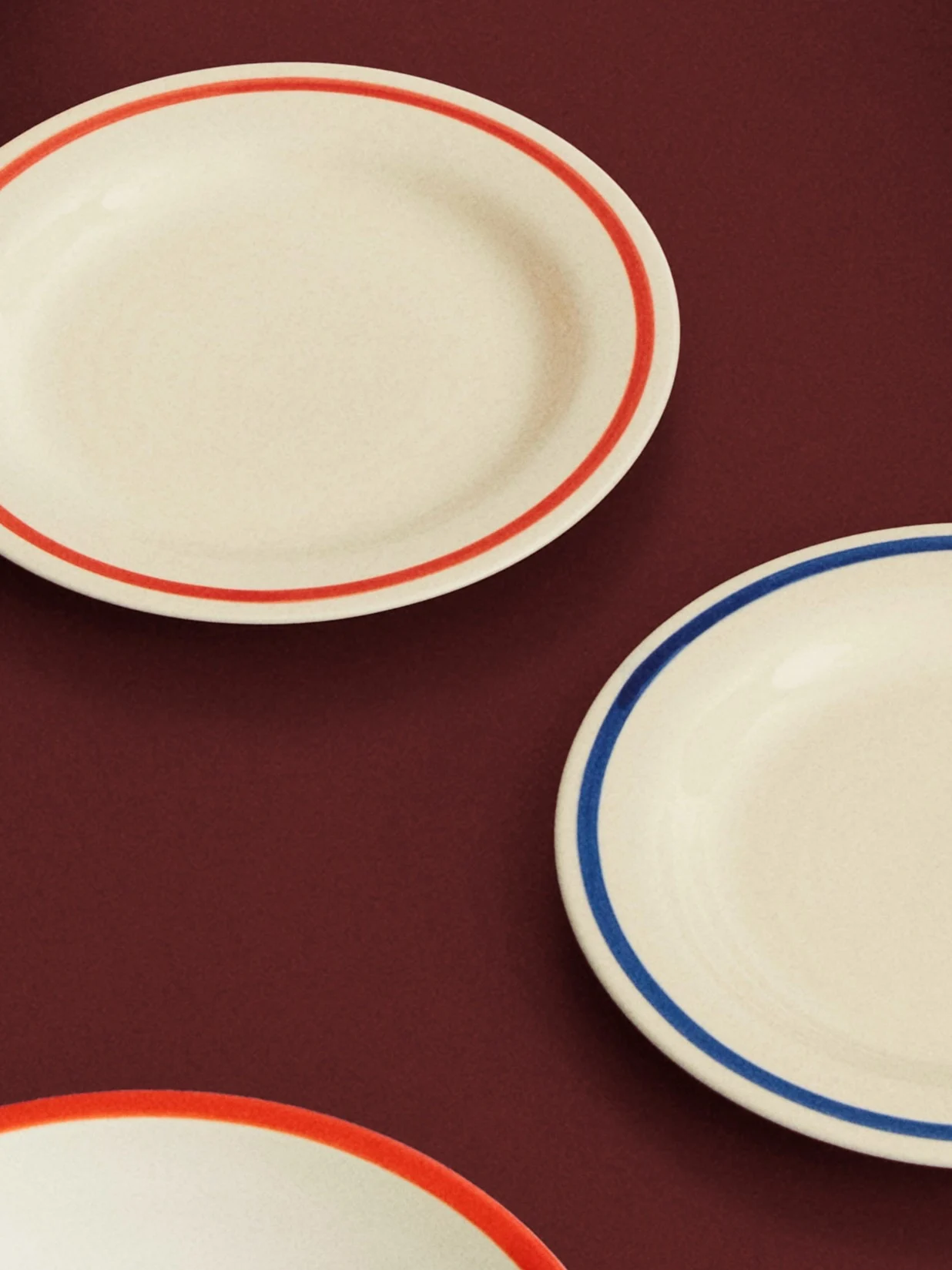 Tres platos ovalados crema con bordes rojos y azules sobre una superficie roja oscura.