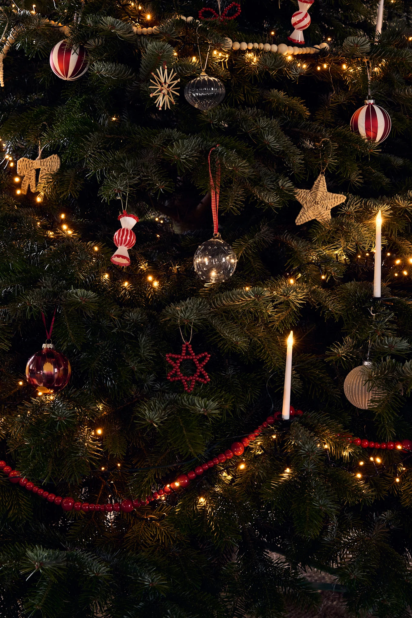 Un árbol de Navidad ricamente decorado con varios adornos, luces cálidas y velas encendidas.