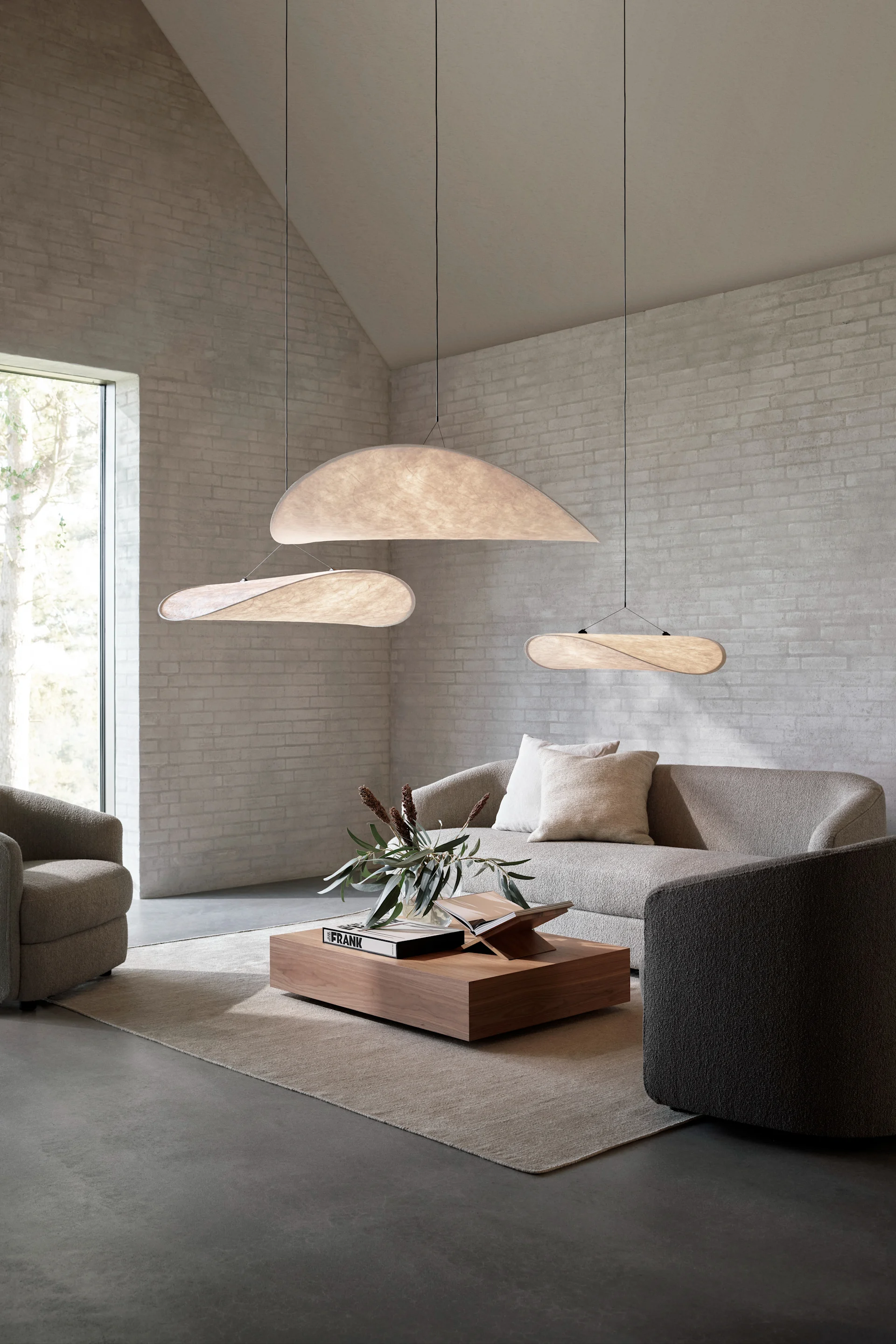 Un gran salón con tres lámparas colgantes Tense que cuelgan en grupo sobre el sofá.