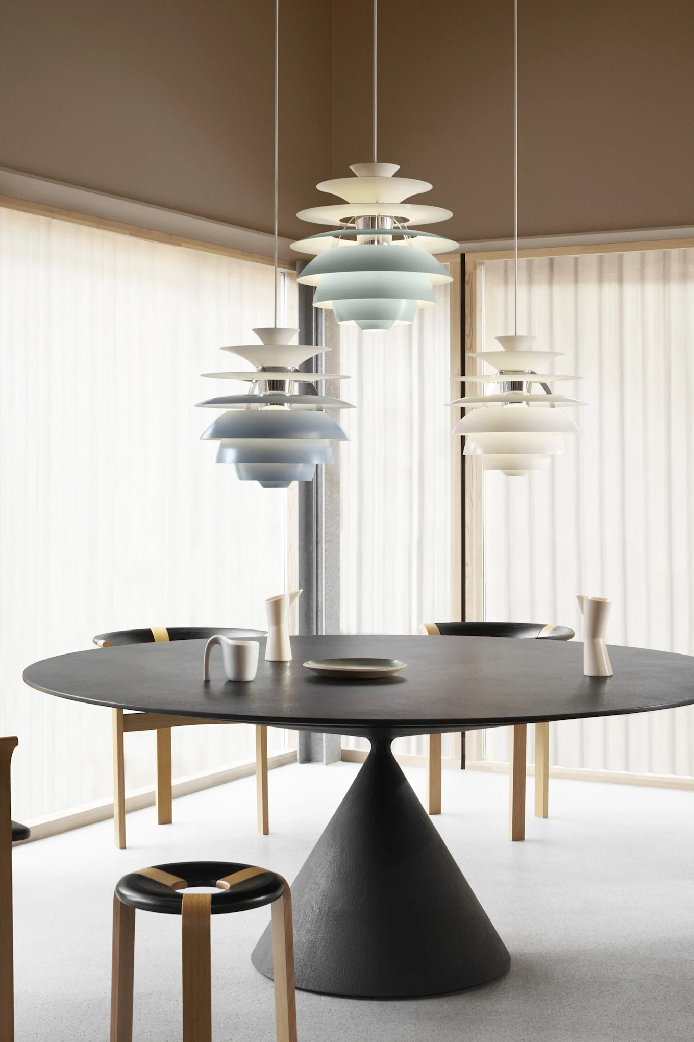 Comedor moderno con mesa redonda negra, sillas y tres lámparas colgantes escalonadas, dos azules y una blanca.