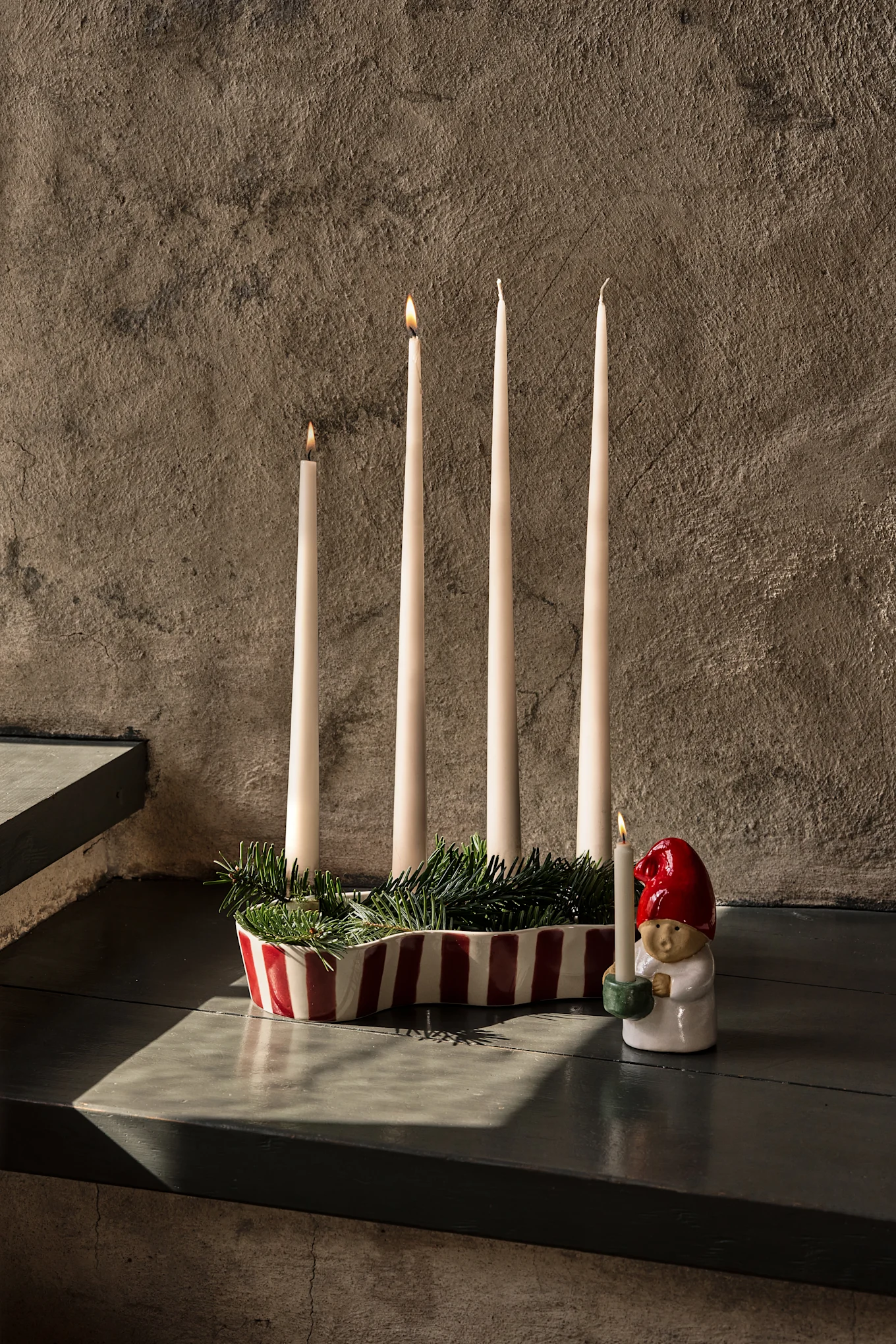 Elegante mesa puesta con tela roja oscura, copas de vino, platos, un frutero escalonado y velas encendidas.