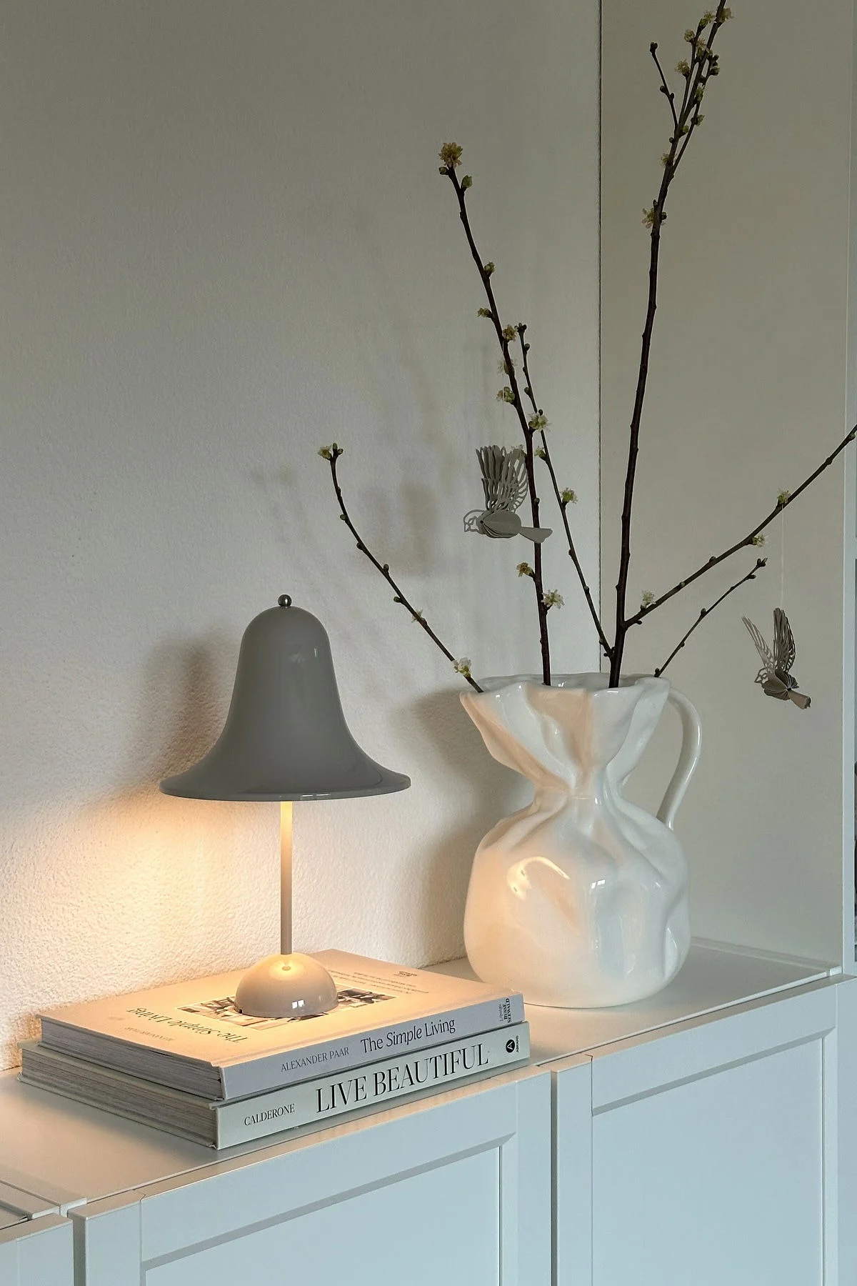 En @oursmall.home puedes ver dos posibles regalos para el Día de la Madre: la lámpara de sobremesa Pantorp, de Verpan, sobre una cómoda; a su lado, el jarrón Crumple, de Byon, con unas ramitas dentro.