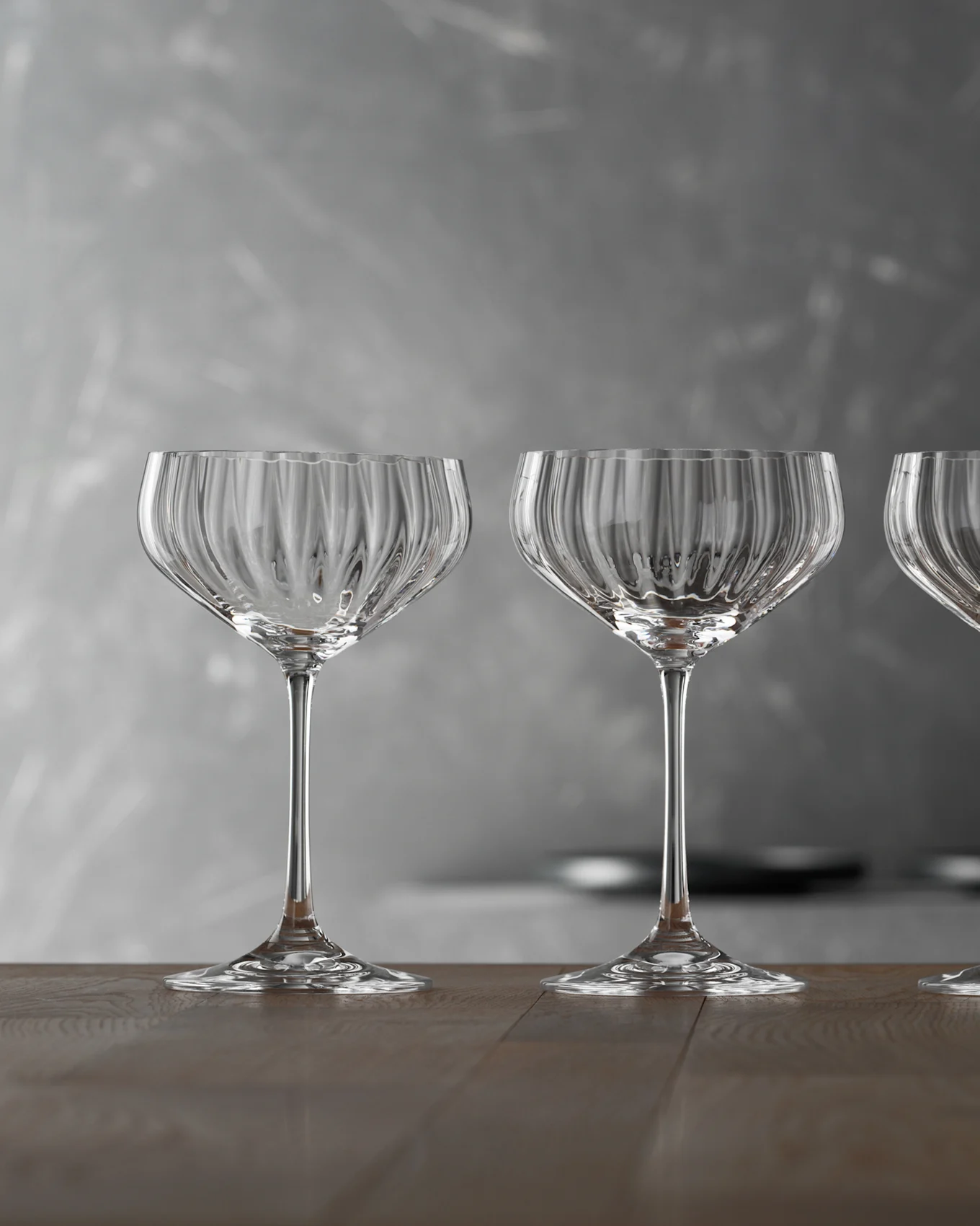 Tres copas de champán vacías, claras y estriadas sobre una mesa de madera con fondo gris.