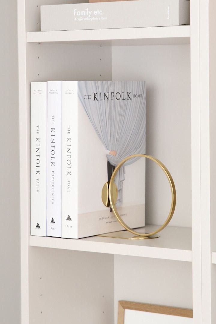 ¿Qué tal un buen libro como regalo para el Día de la Madre? Regala un sujetalibros a juego, como el anillo dorado para libros de Cooee Design, que aparece aquí en una estantería.