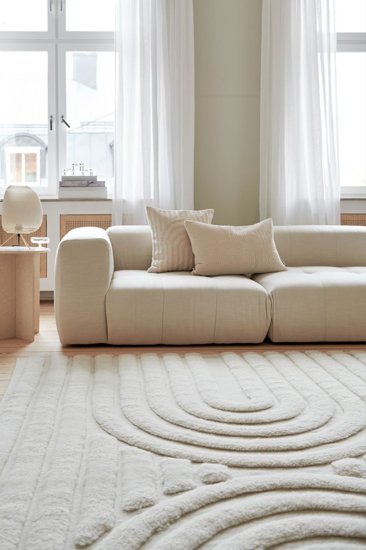 Alfombras para el salón: la alfombra de lana Curve en tonos claros de Classic Collection está colocada frente a un sofá en un salón luminoso y lleno de luz natural.