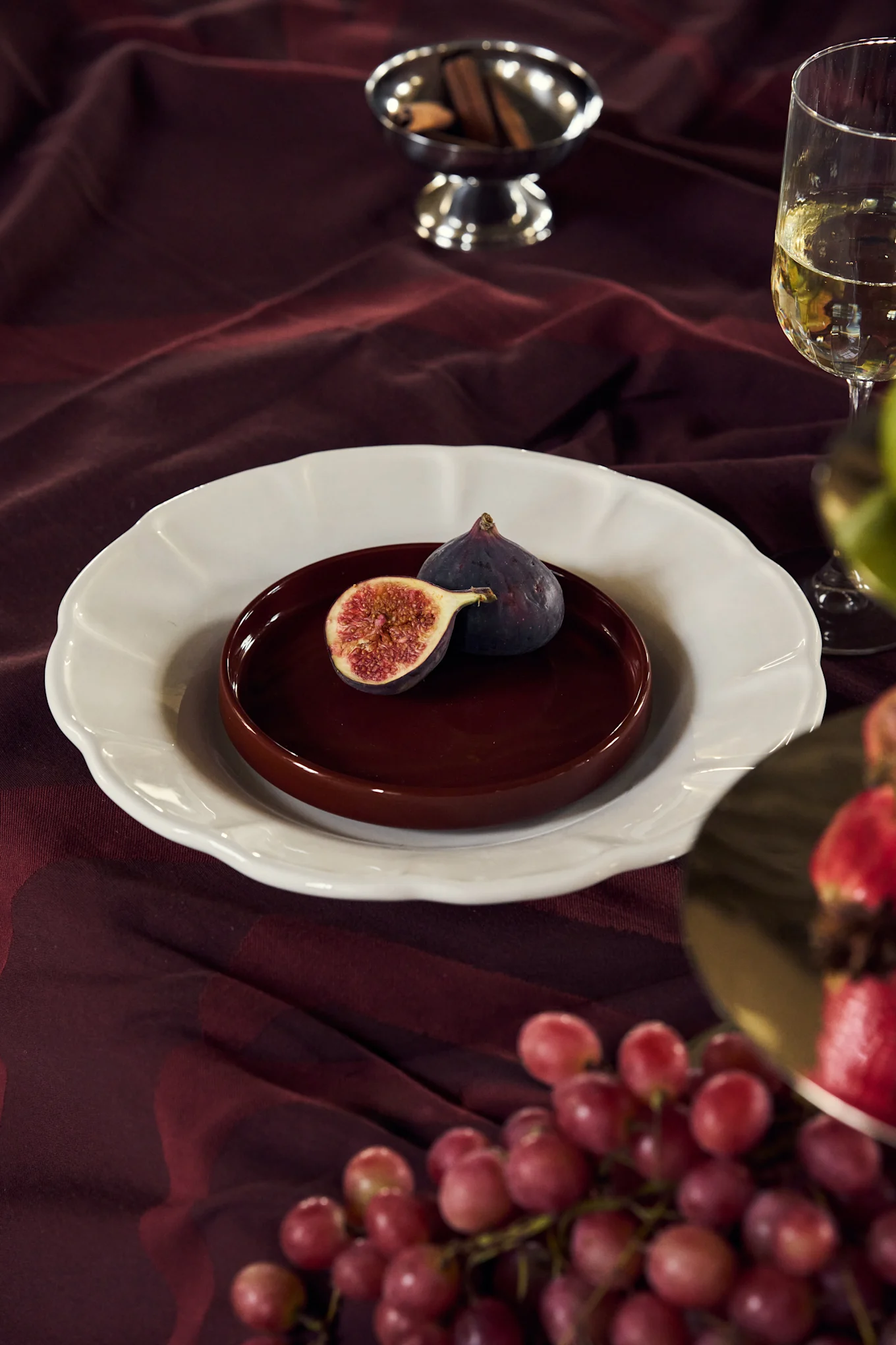 Higos en un plato sobre un mantel burdeos con vino, uvas y ramas de canela.