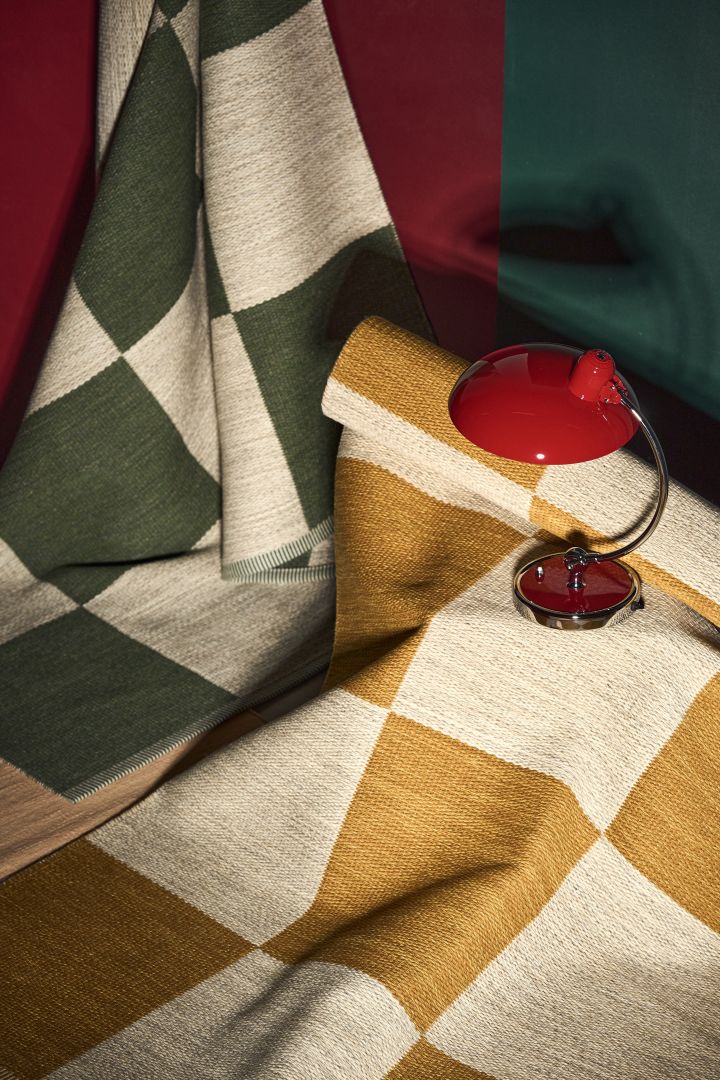 Las alfombras con patrones geométricos en amarillo mostaza/blanco y verde/blanco son perfectas para las tendencias de diseño de interiores escandinavas en 2024, aquí con una lámpara de mesa roja junto a ellas.