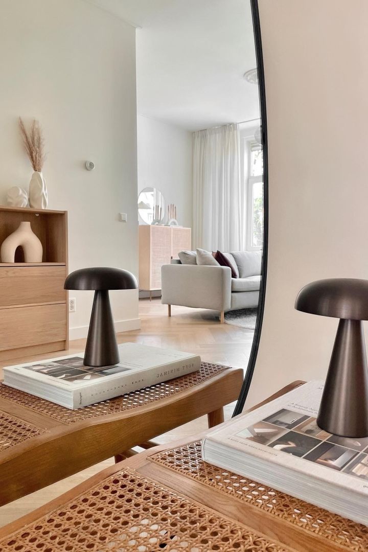 Aquí puedes ver la lámpara portátil Como de &tradition colocada sobre un libro en una sala de estar de estilo Japandi limpia y despejada.