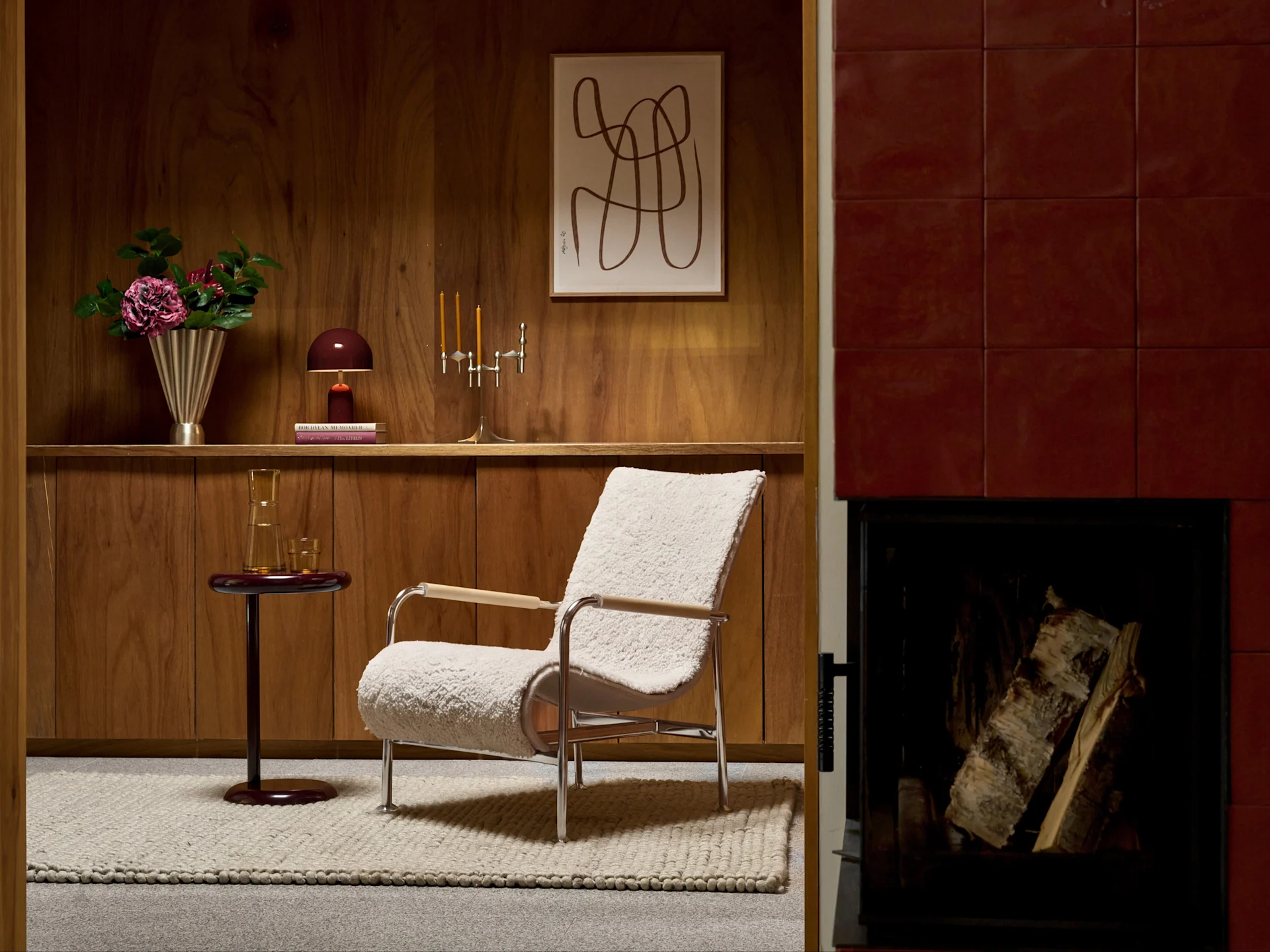 Un sillón bouclé crema con marco cromado en una habitación con paneles de madera, junto a una chimenea roja.