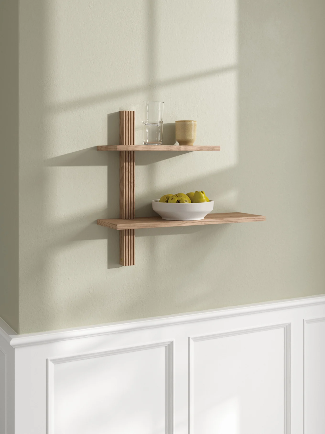 Estante de pared de madera de dos niveles con soporte de celosía, con un vaso, una taza y un cuenco de fruta verde-amarilla.