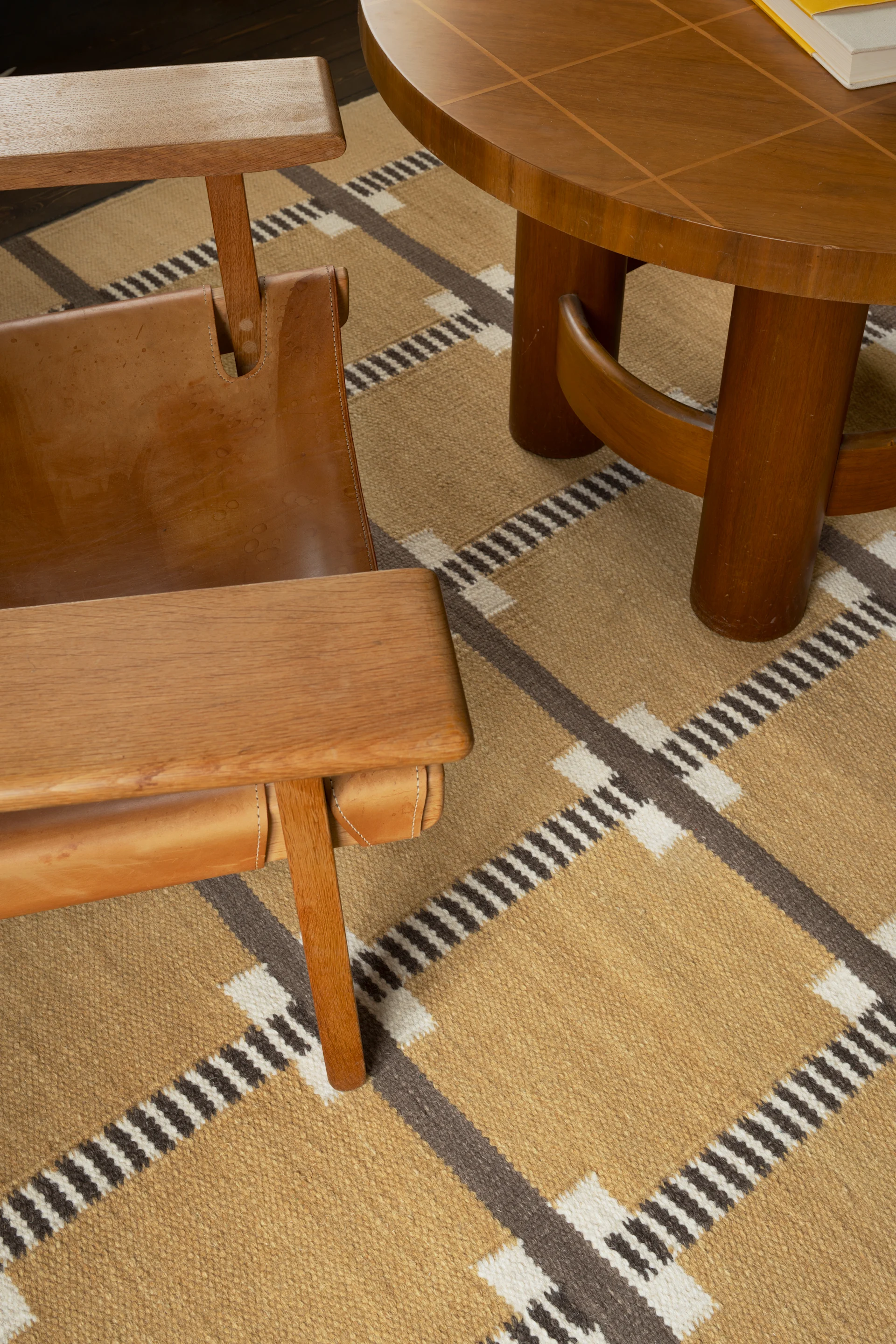 Sillón de madera con asiento de cuero junto a una mesa de centro redonda sobre una alfombra con patrón geométrico.