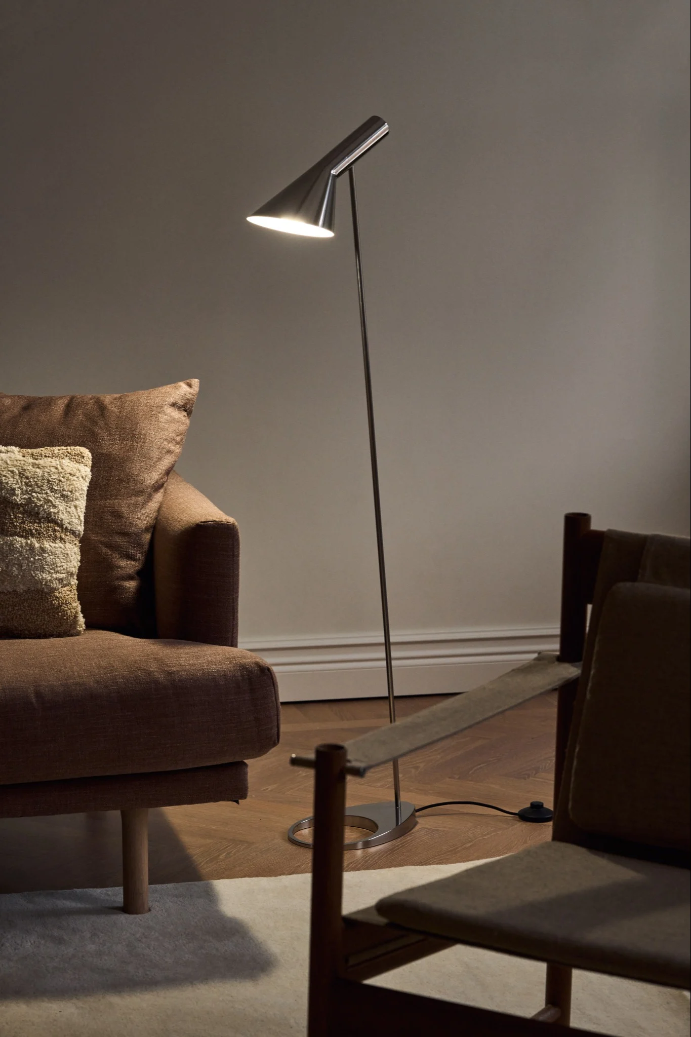 Lámparas escandinavas: la lámpara de pie AJ de Louis Poulsen en acabado cromado está en un salón sencillo, junto a un sofá.