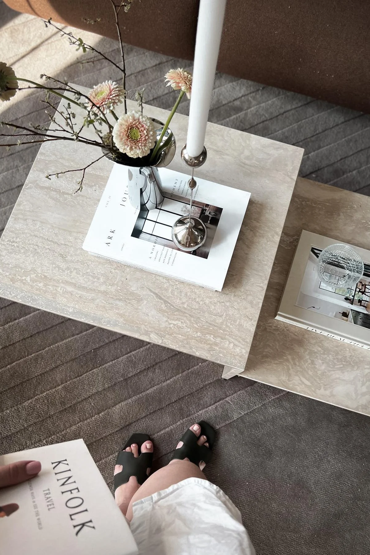 La mesa auxiliar Distinct de Ferm Living está decorada con un libro, el candelabro Tender de Klong y el jarrón Bloom Botanica con flores frescas.