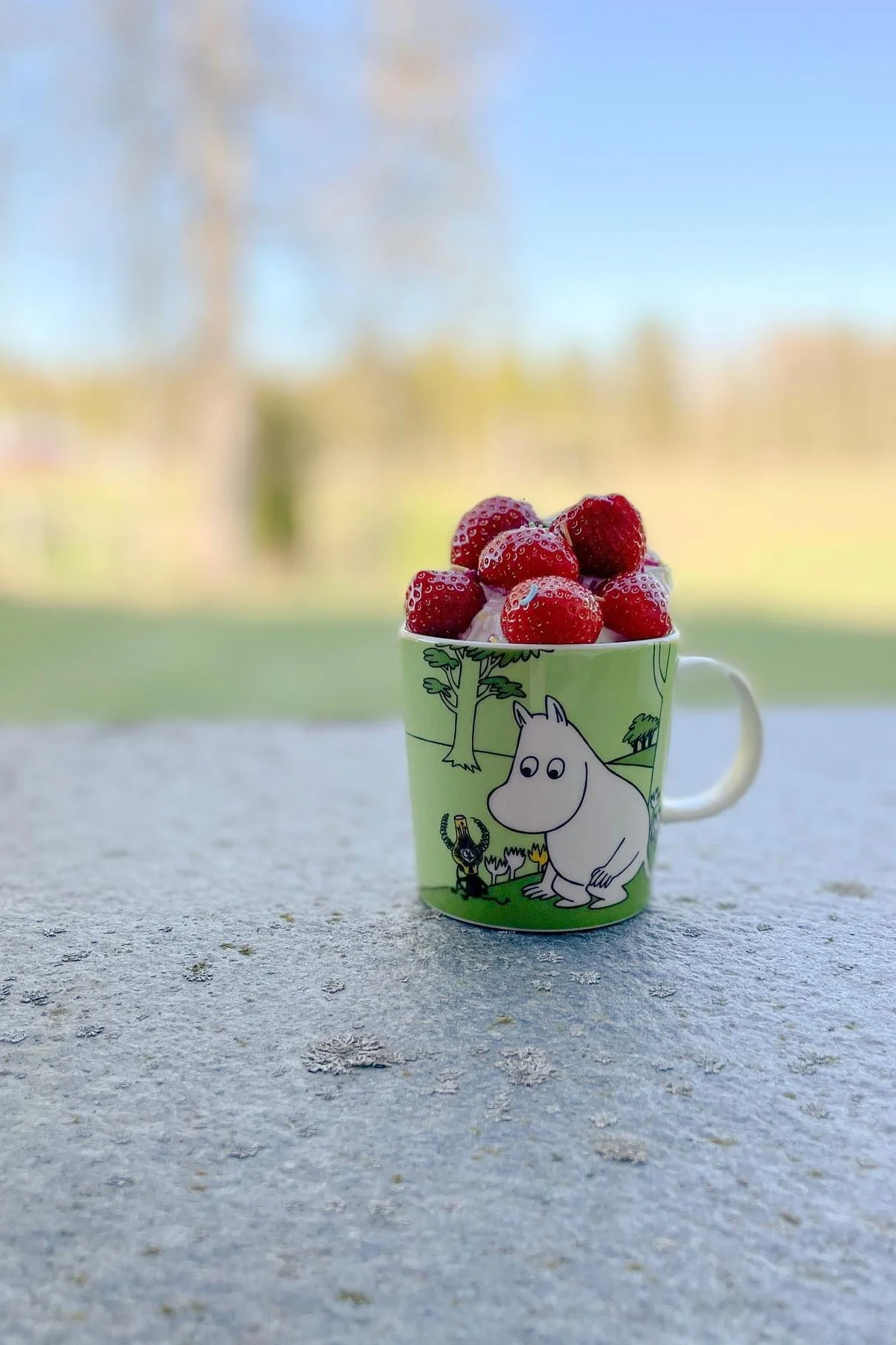 La taza verde Moomin de @mylittlemoominfamily está en el suelo, llena de fresas.