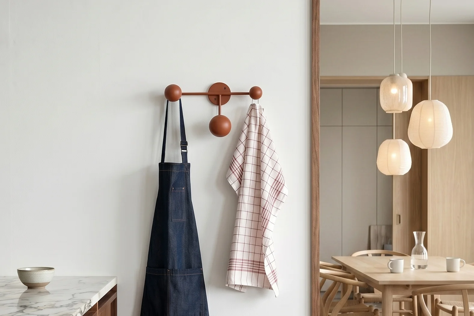 Cocina con mármol. Delantal azul, paño a cuadros en perchero. Comedor con mesa y lámparas colgantes.