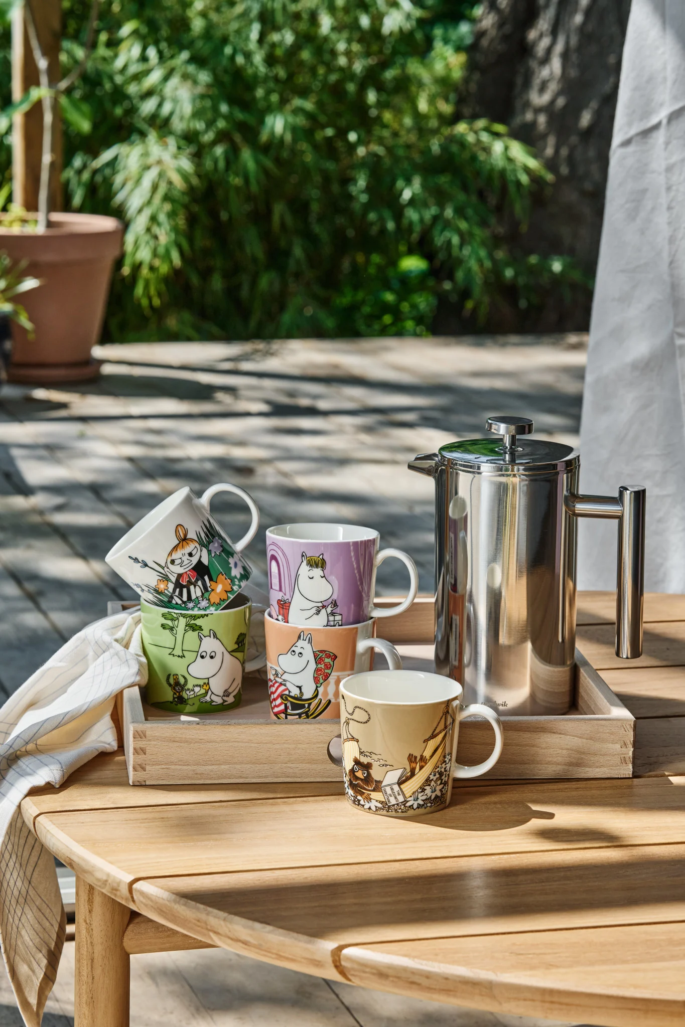 Varias tazas de Mumin están sobre una mesa en el jardín.