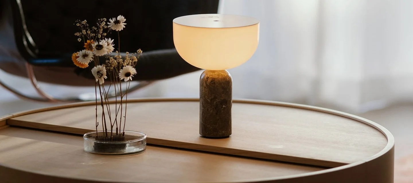 La mesa de centro Arc de Woud está decorada con una lámpara de mesa Kizu de New Works y el erizo para flores Garden Glory.