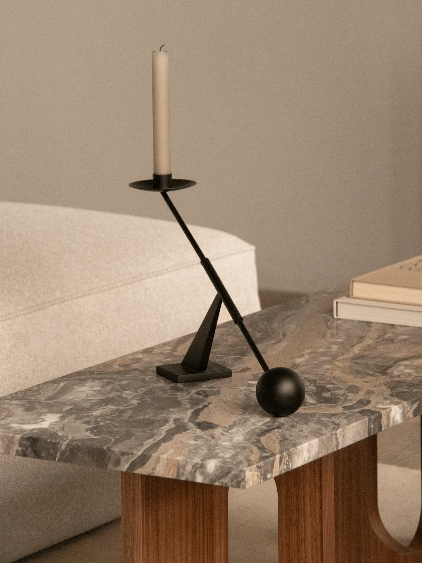 Un candelabro moderno negro con una vela blanca sobre una mesa de centro de mármol junto a dos libros y un sofá claro.