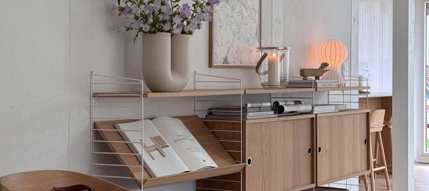 Estantería modular con marcos blancos, estantes, armarios de madera, jarrón con flores, farol y lámpara de seta.