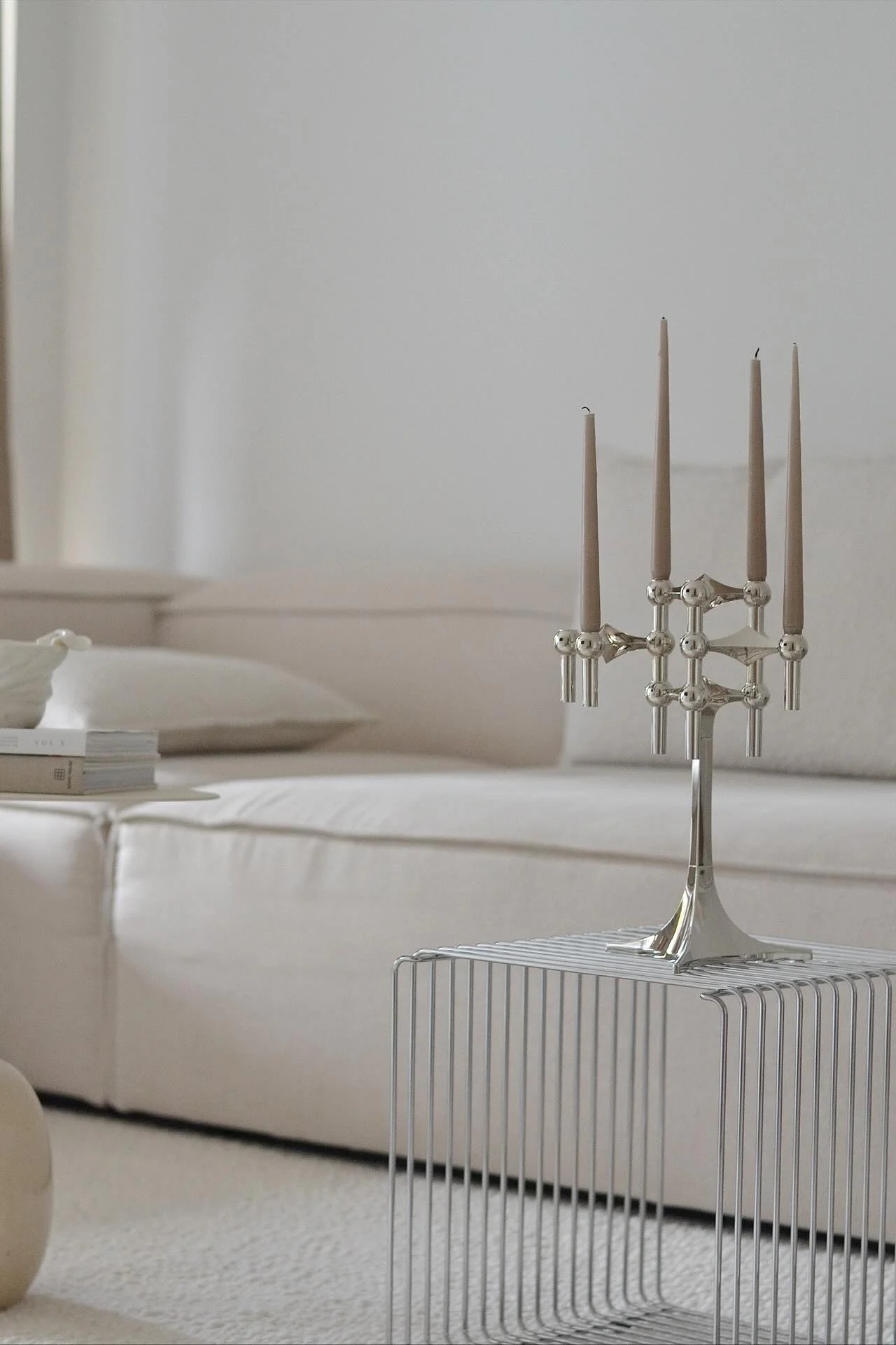 Un candelabro plateado con cinco velas marrones claras se apoya sobre una mesa auxiliar de metal minimalista. Un sofá claro está en el fondo.