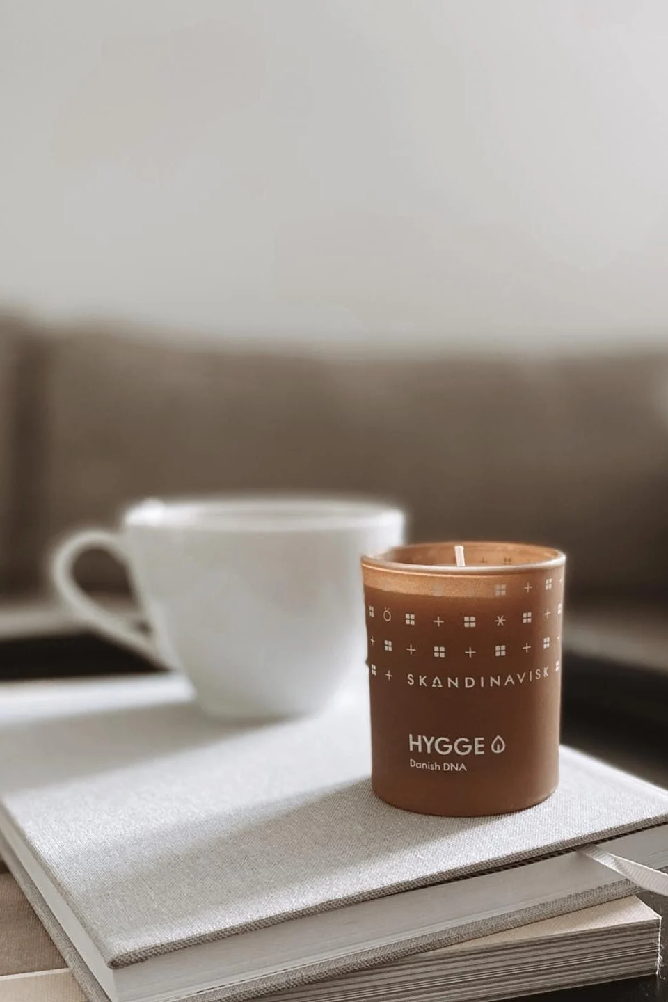 Una vela aromática como la Hygge de Skandinavisk, que aquí se muestra sobre una pila de libros en la mesa de centro, es un regalo perfecto para San Valentín y para disfrutar de veladas acogedoras.