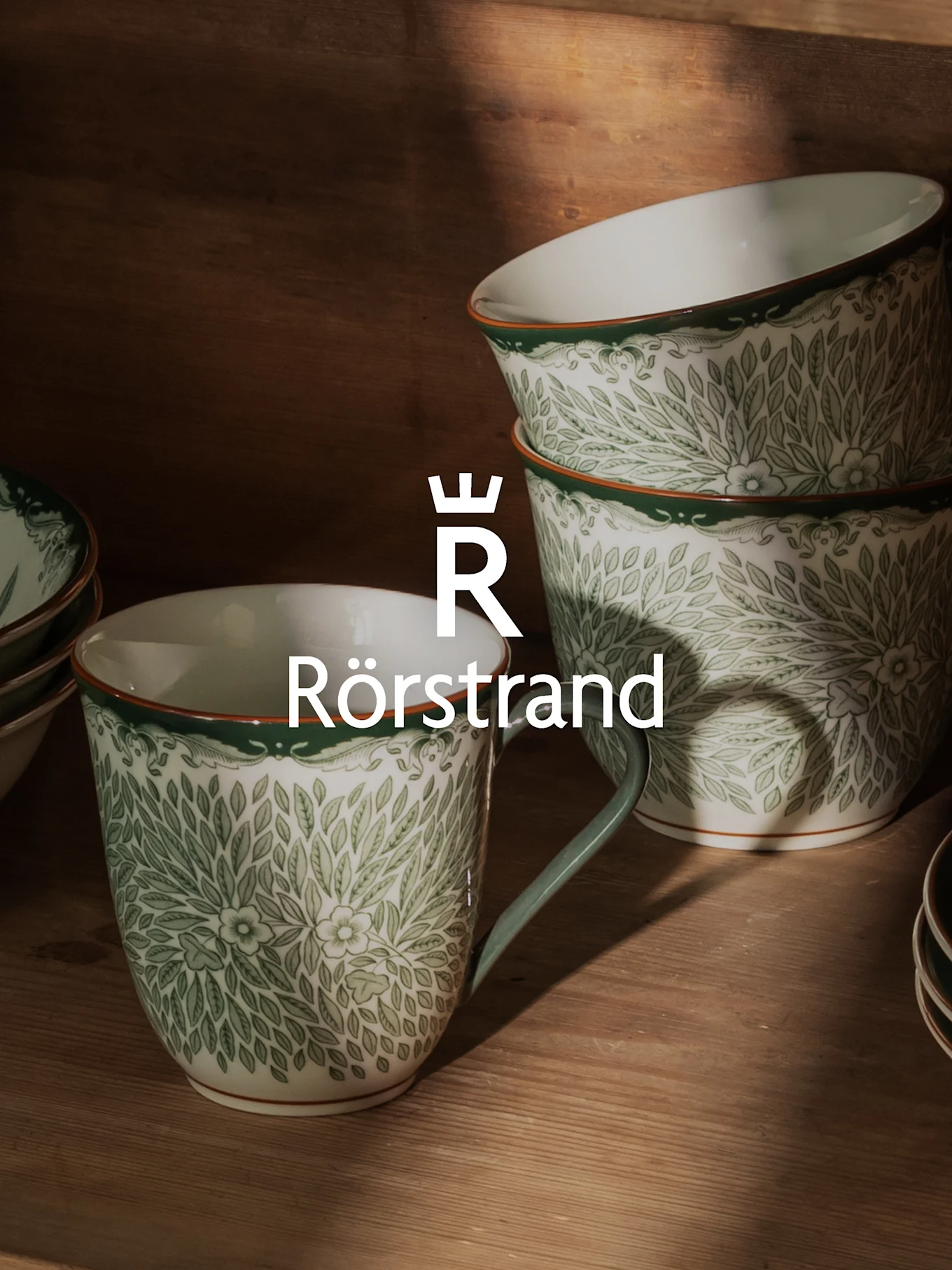 Tazas y cuencos de cerámica blancos con patrón de hojas verdes, borde naranja y logo Rörstrand.