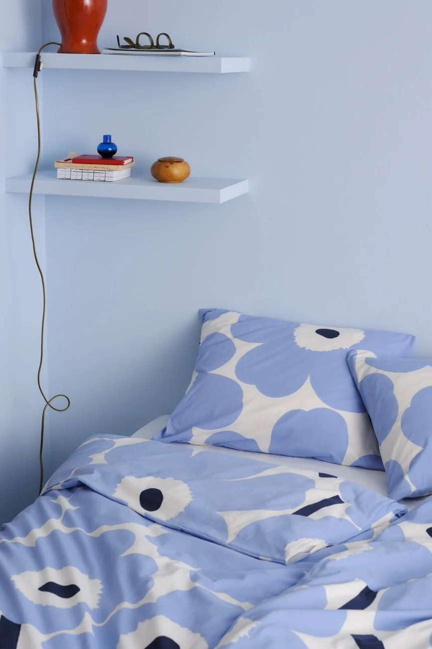 Una esquina de dormitorio con paredes azules claras, dos estantes flotantes y una cama con ropa de cama floral azul y blanca.